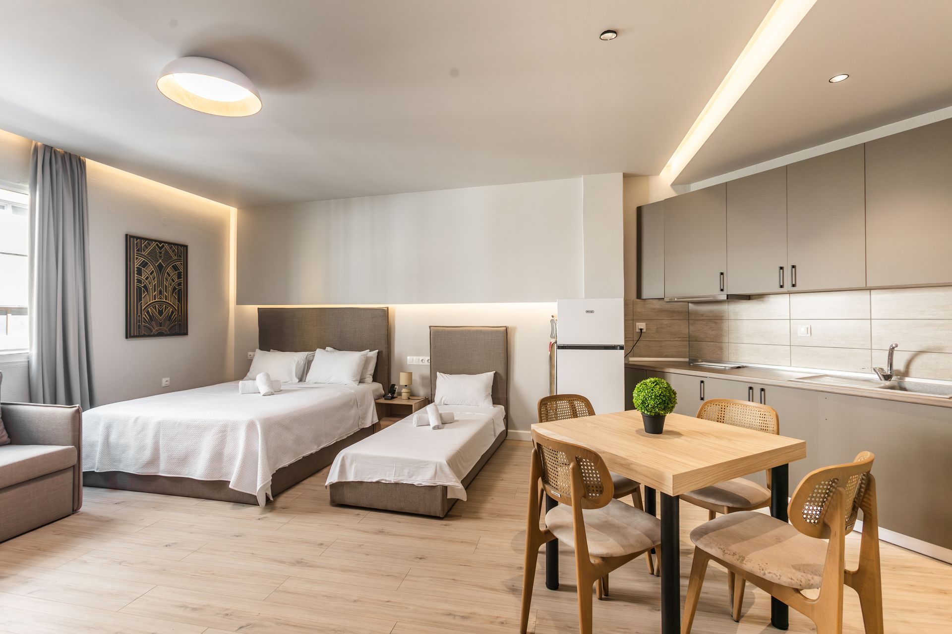 Studio apartment with beds, kitchen, dining table, and sofa. Modern decor, light colors.