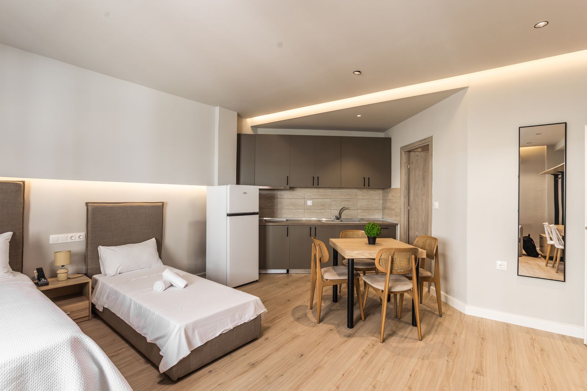 Modern studio apartment with two beds, kitchenette, dining area, and a tall mirror.