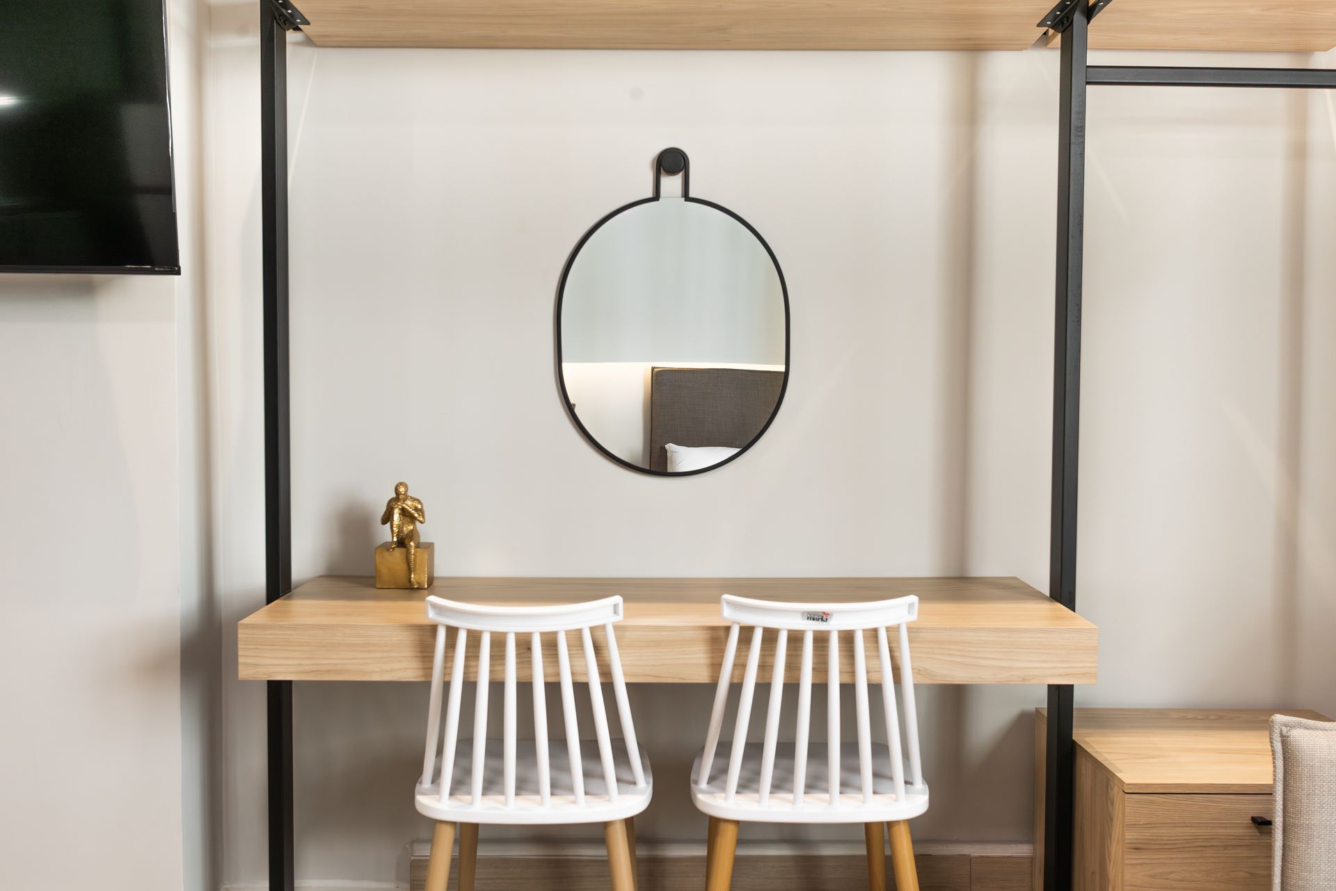 Desk with two white chairs, a mirror, and shelves, set against a white wall.