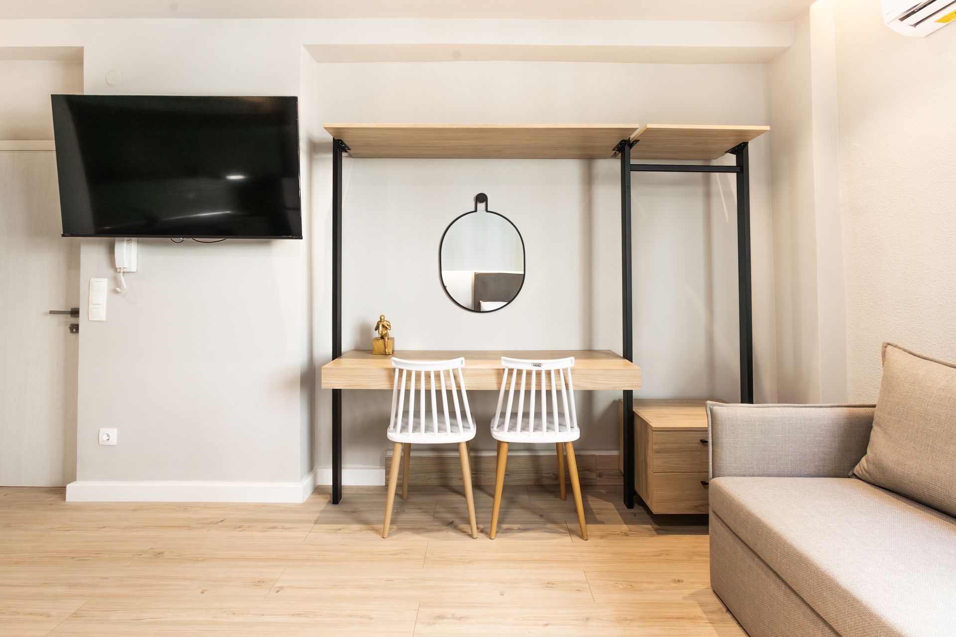 Modern room with desk, chairs, TV, and couch. Neutral colors and minimalist design.