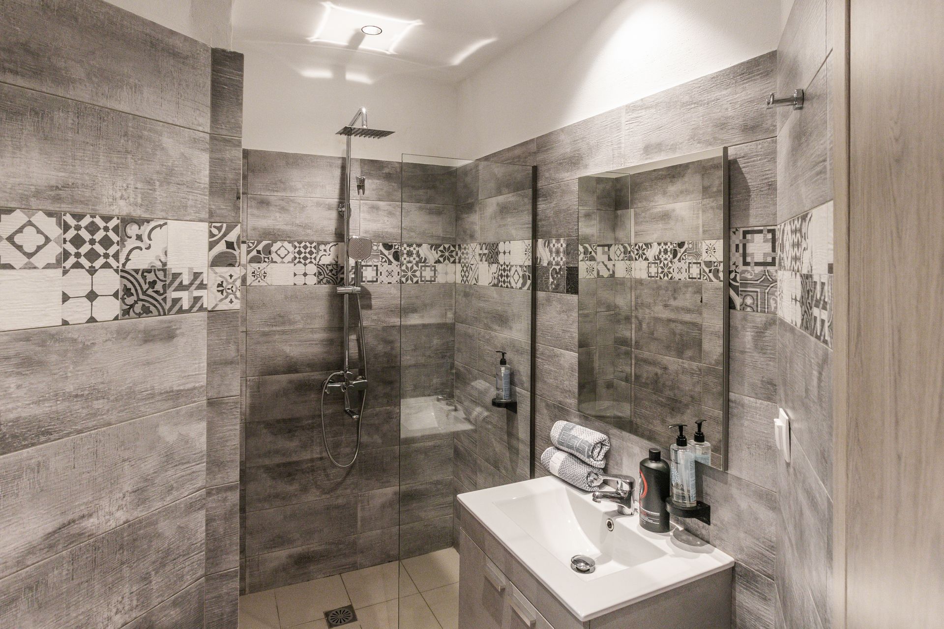 Modern bathroom with gray tiled walls, shower, vanity, and decorative tile accents.