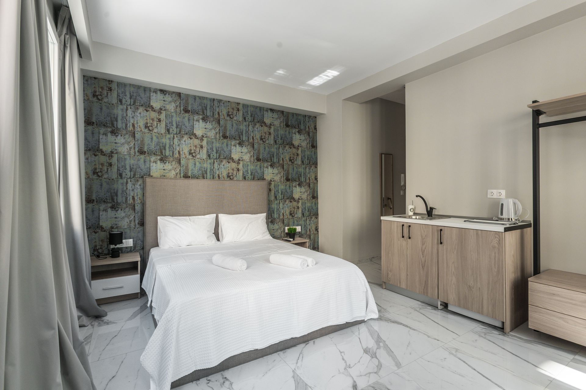 Bedroom with a bed, kitchenette, and wardrobe against a textured accent wall and marble flooring.