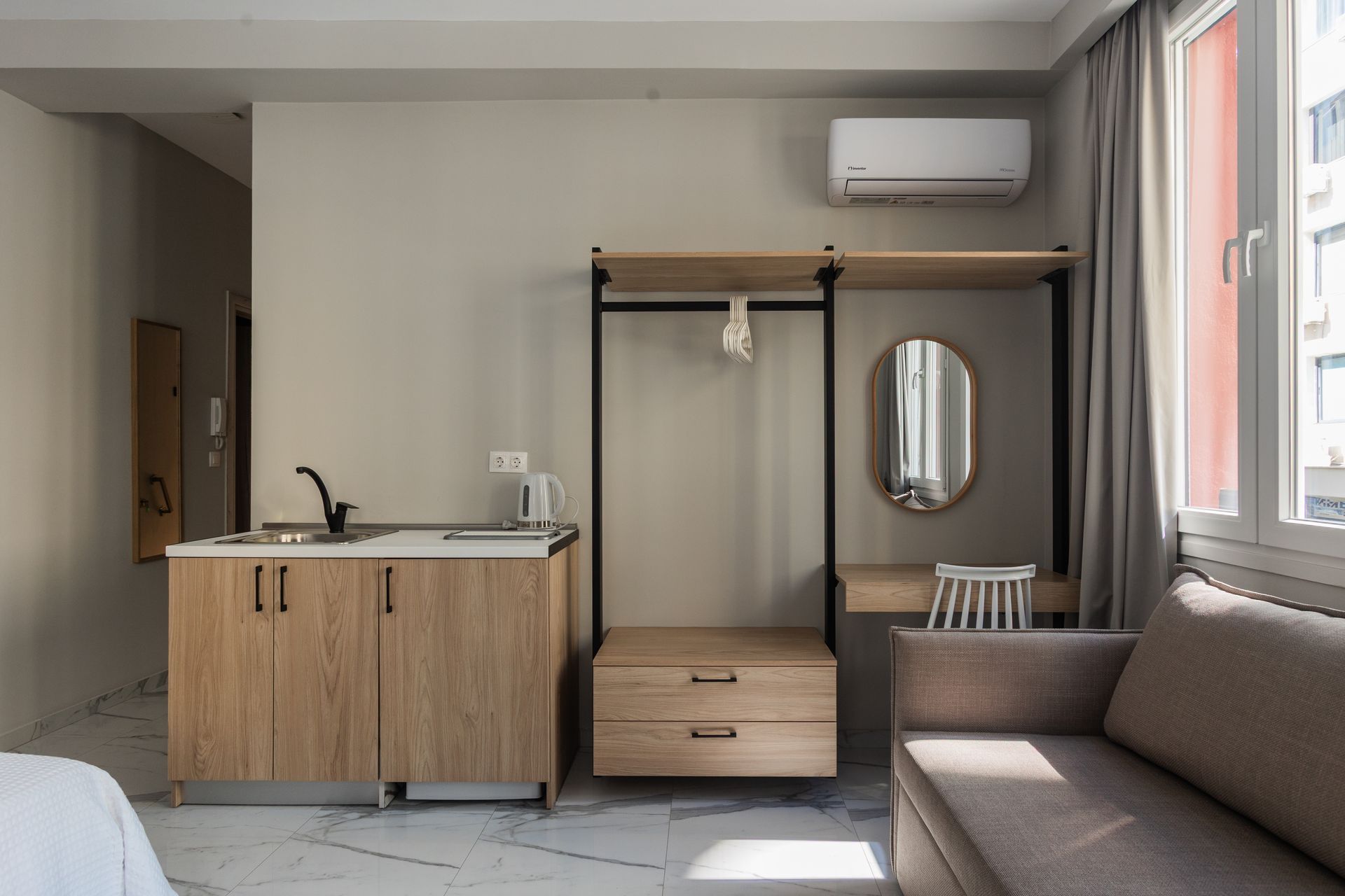 Studio apartment with kitchenette, closet, sofa, and window; neutral tones.