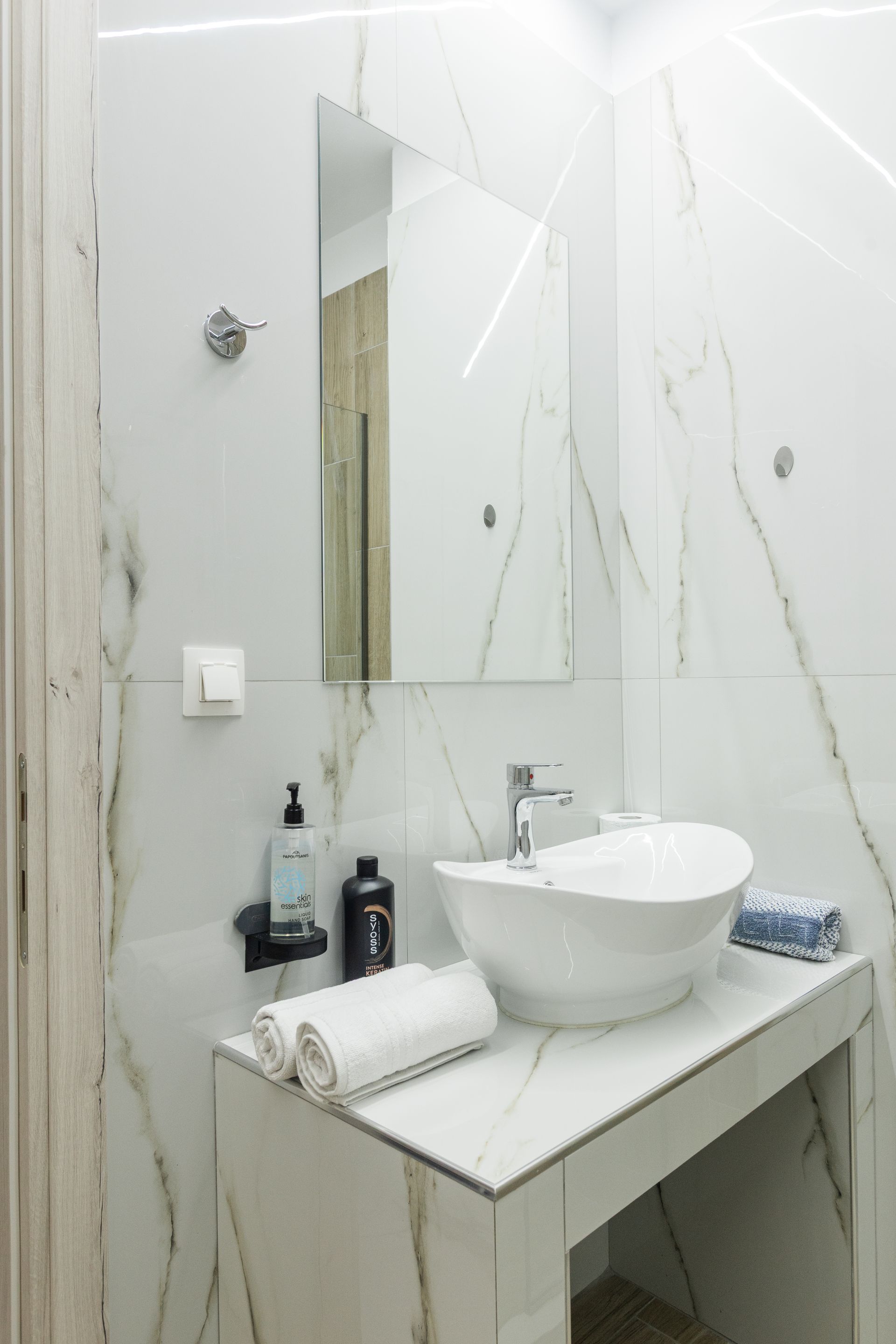 Modern bathroom with white marble-look walls, vessel sink on a counter, mirror, and toiletries.