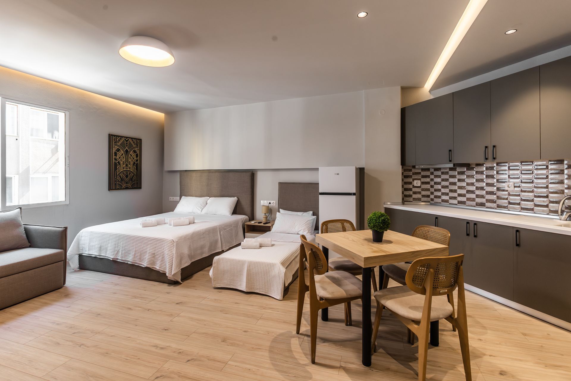 A modern studio apartment with beds, a small kitchen, dining table, and a sofa.