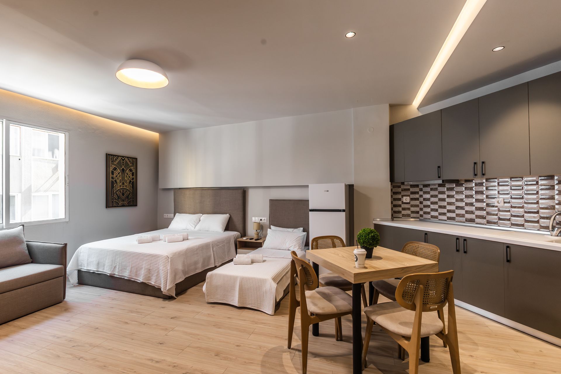 Modern studio apartment with two beds, kitchenette, dining table, and a small sofa.