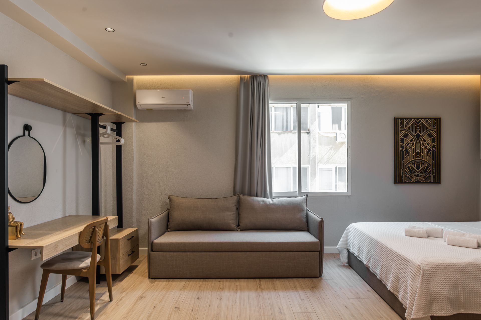 Cozy studio apartment with a bed, sofa, desk, and window. Light wood and gray accents.