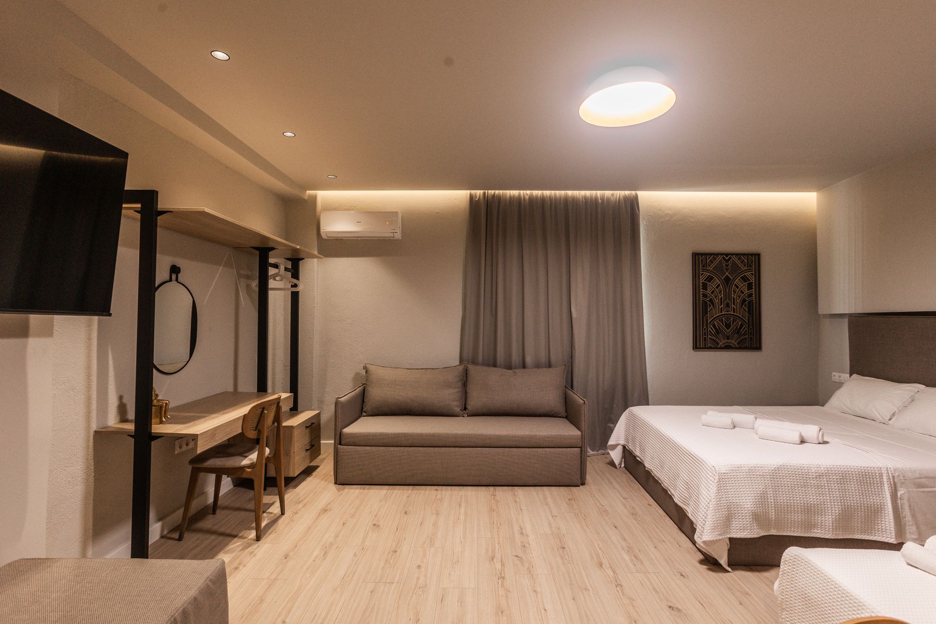 Hotel room with a bed, sofa, desk, and TV. Neutral colors, modern design.