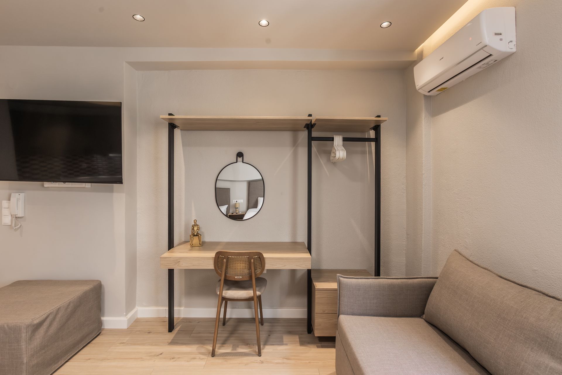 Modern hotel room with desk, mirror, closet, TV, sofa, and air conditioning.