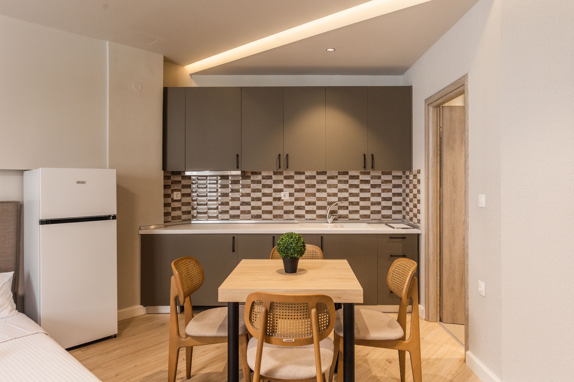 Small kitchen with a dining table and fridge. Dark gray cabinets and tiled backsplash.