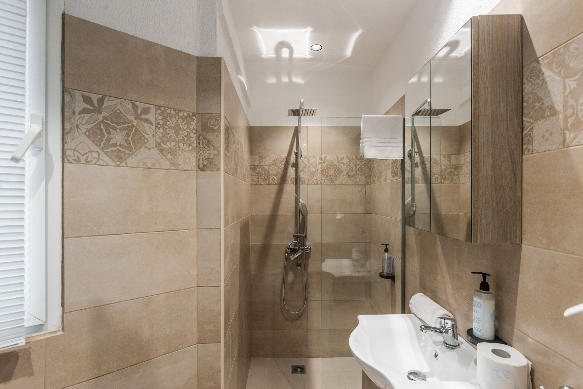 Bathroom with shower, sink, and decorative tile. Beige tones throughout.