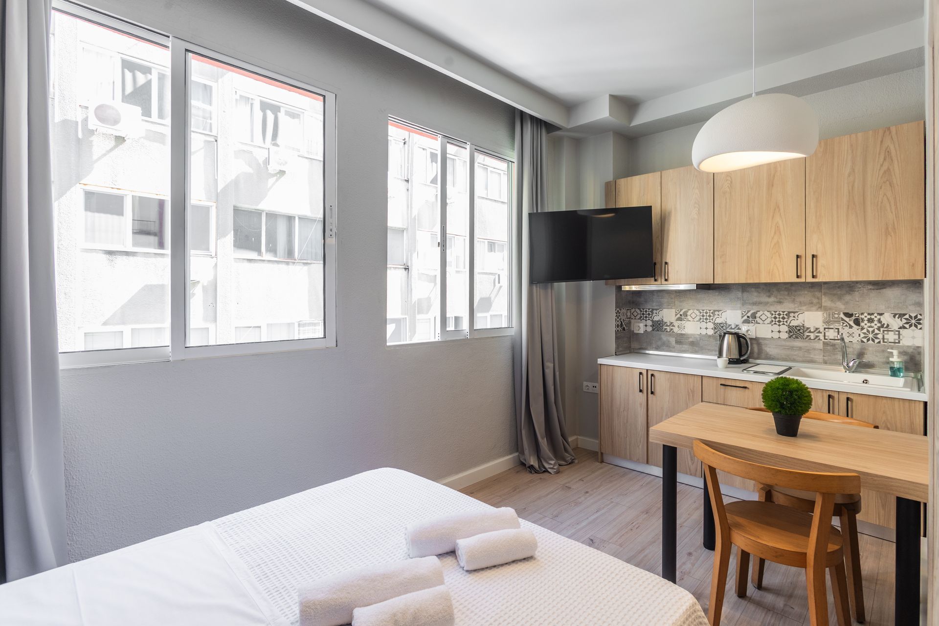 Small apartment with a bed, kitchen, table, and large windows.