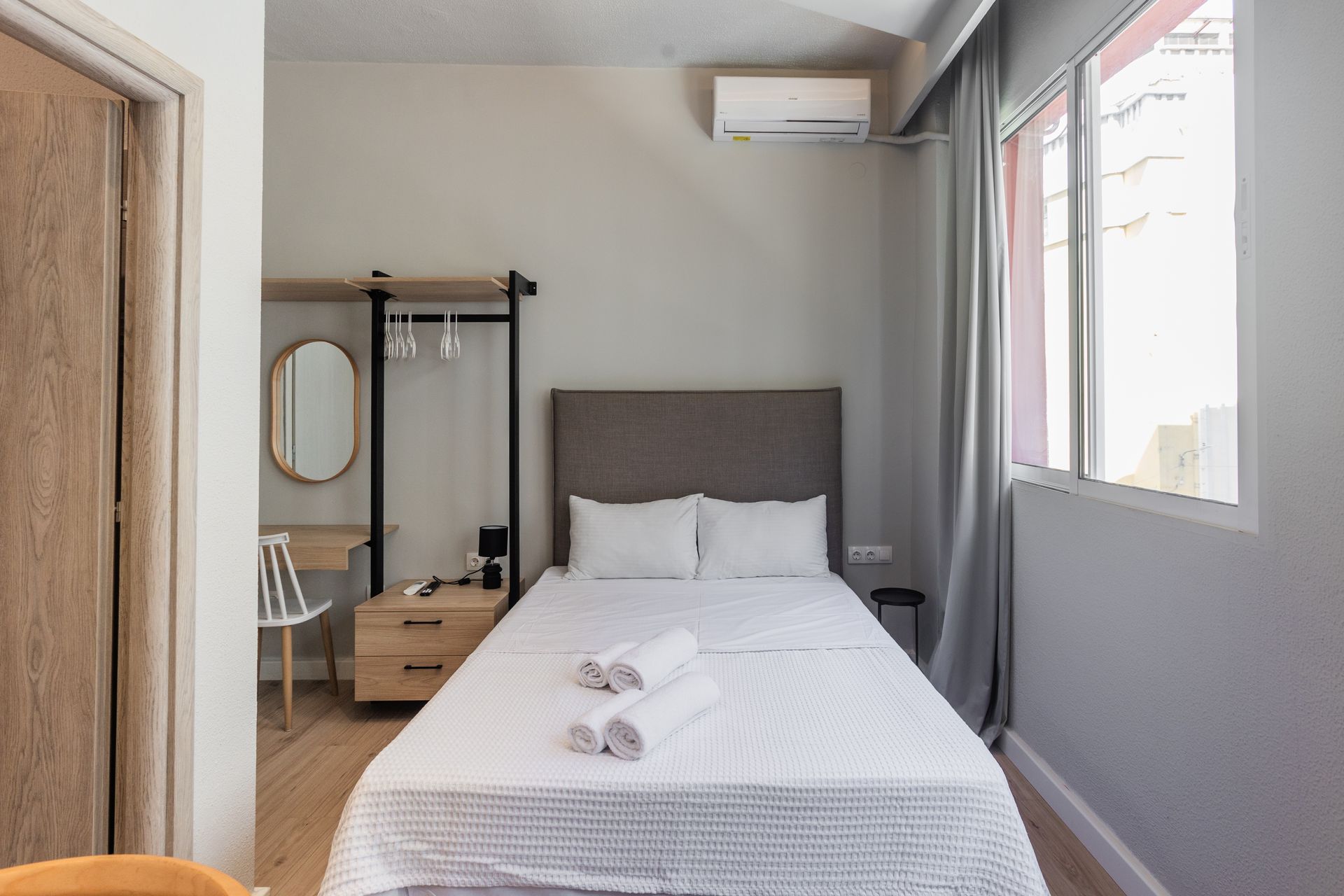 Bedroom with a bed, dresser, hanging rack, and window; gray and wood tones.