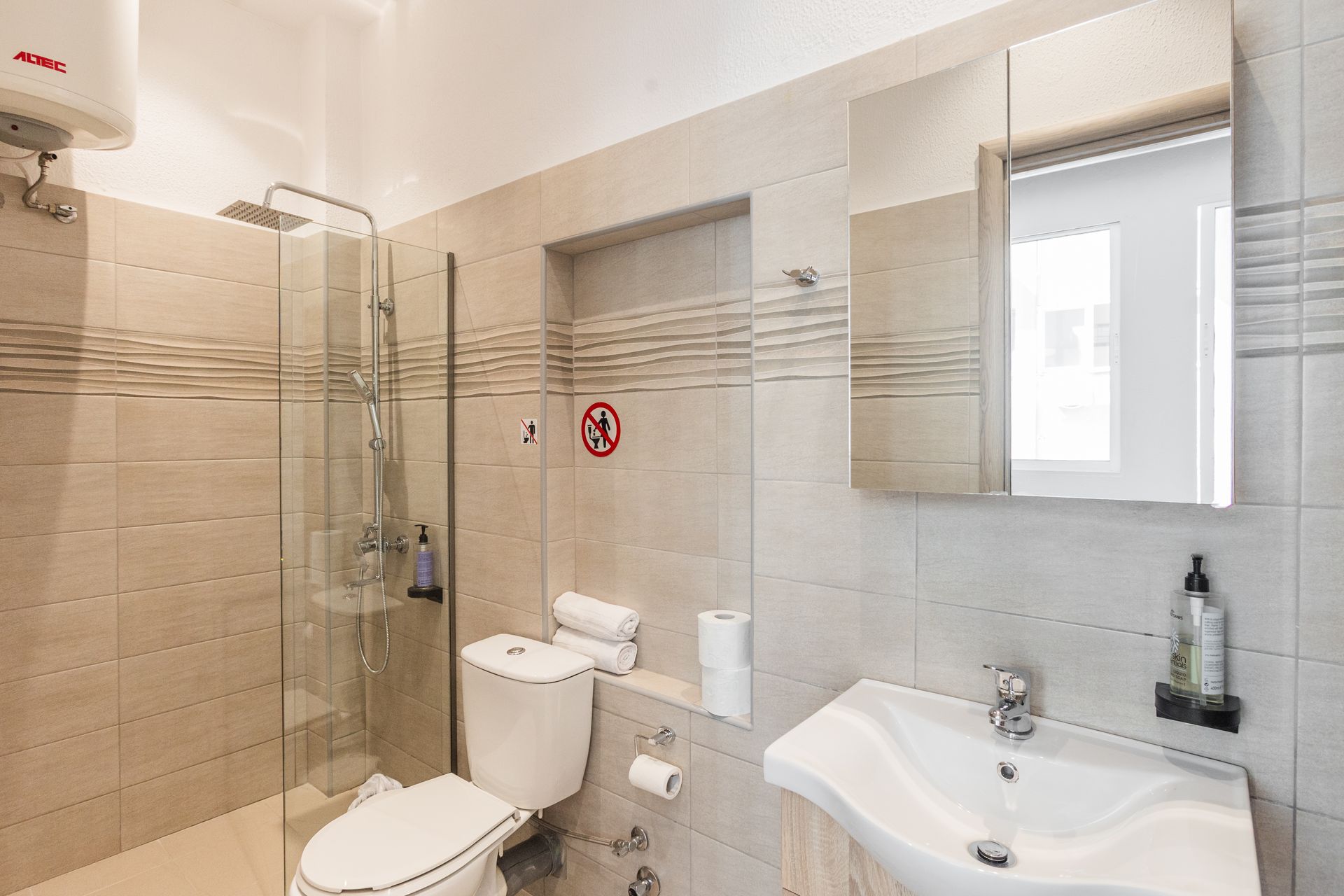 Small, tiled bathroom with a glass shower, toilet, sink, and mirror.