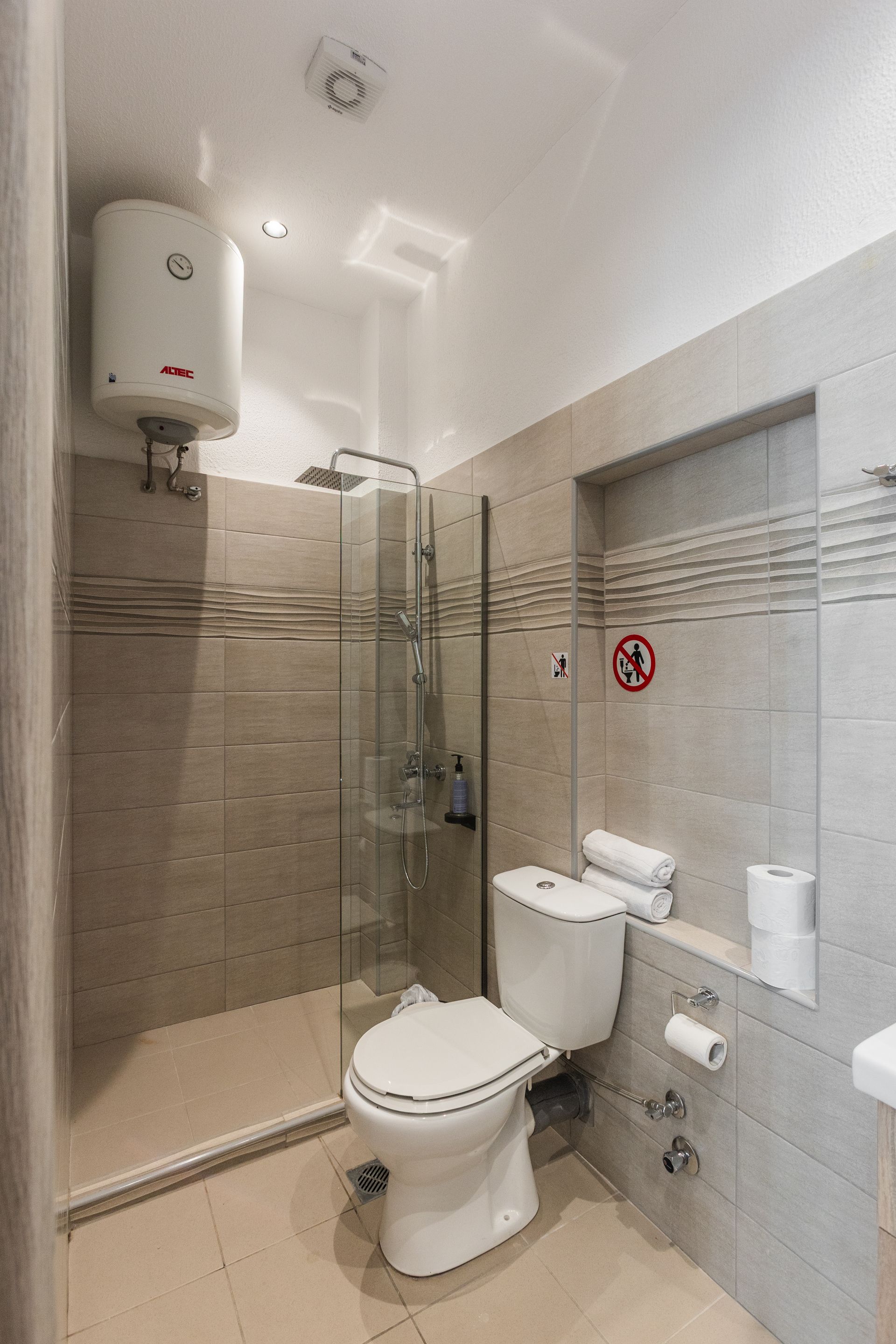 Bathroom with toilet, shower, and water heater; light tan tiles.