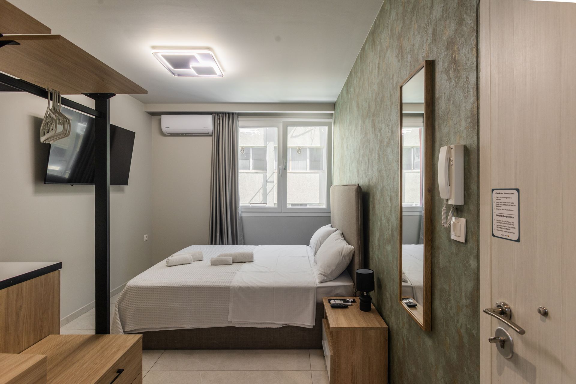 Small hotel room with bed, window, TV, and decorative wall.