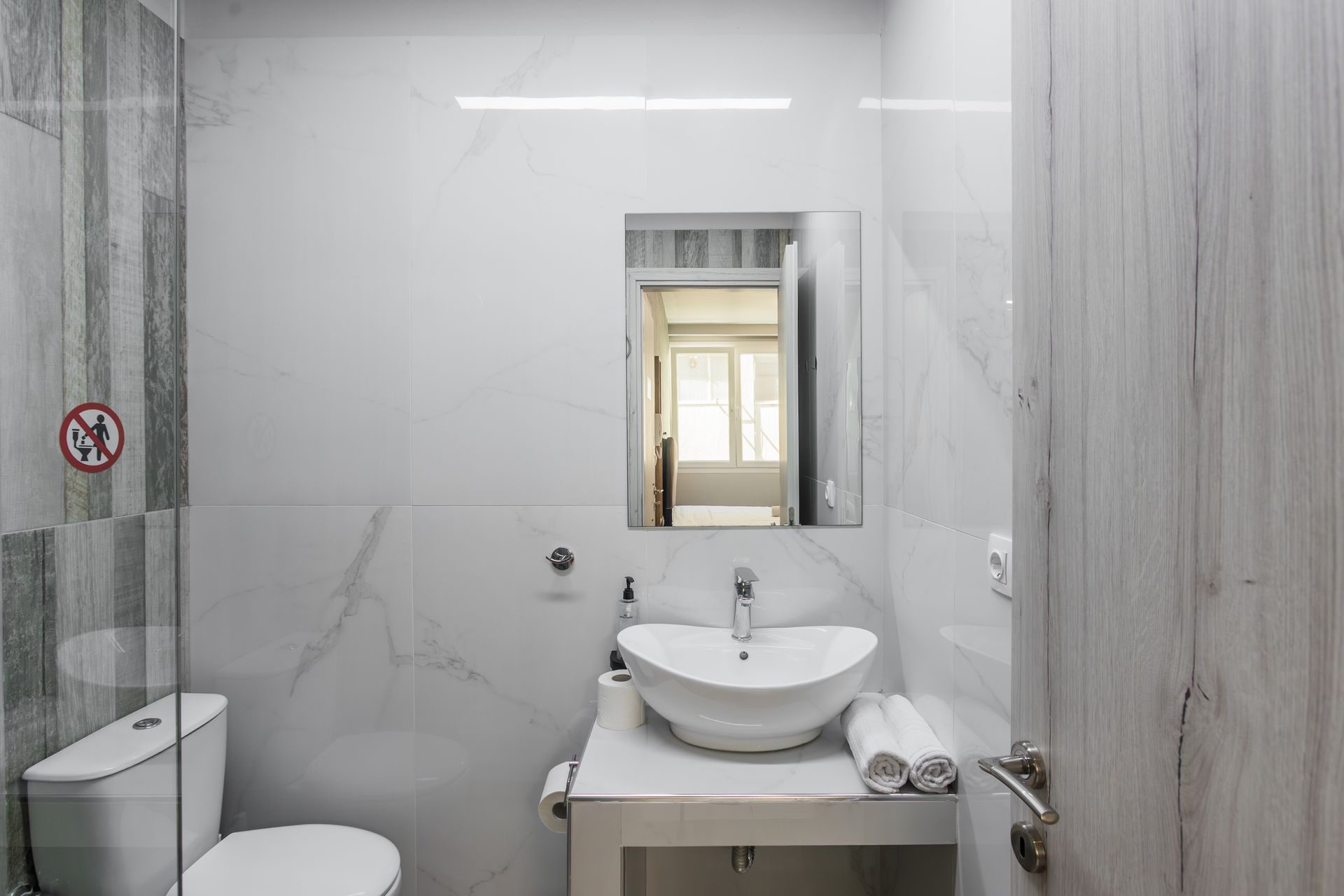 Bathroom with white sink, marble wall, toilet, and open wooden door.