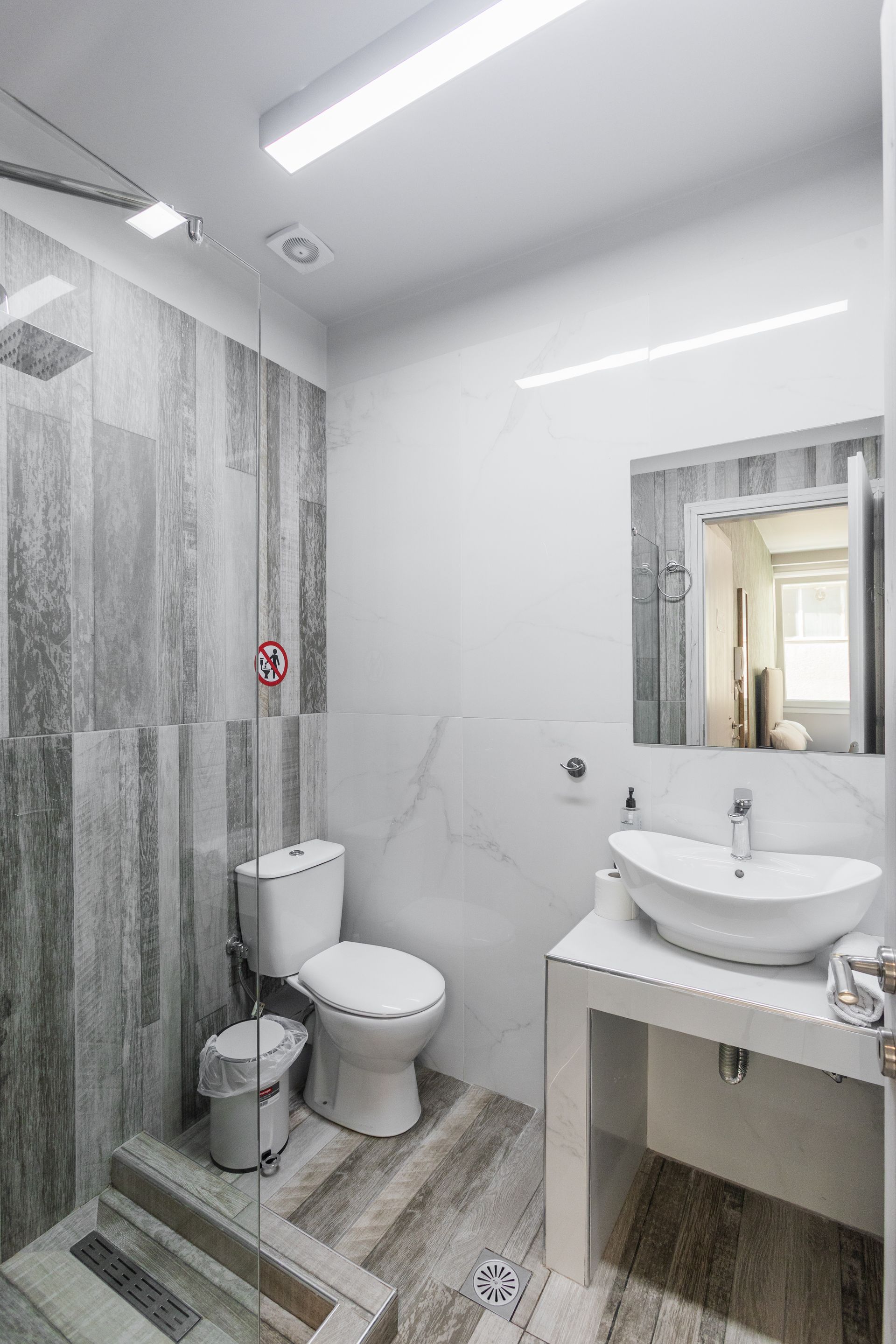 Bathroom with gray and white tile, shower, toilet, sink, and mirror.