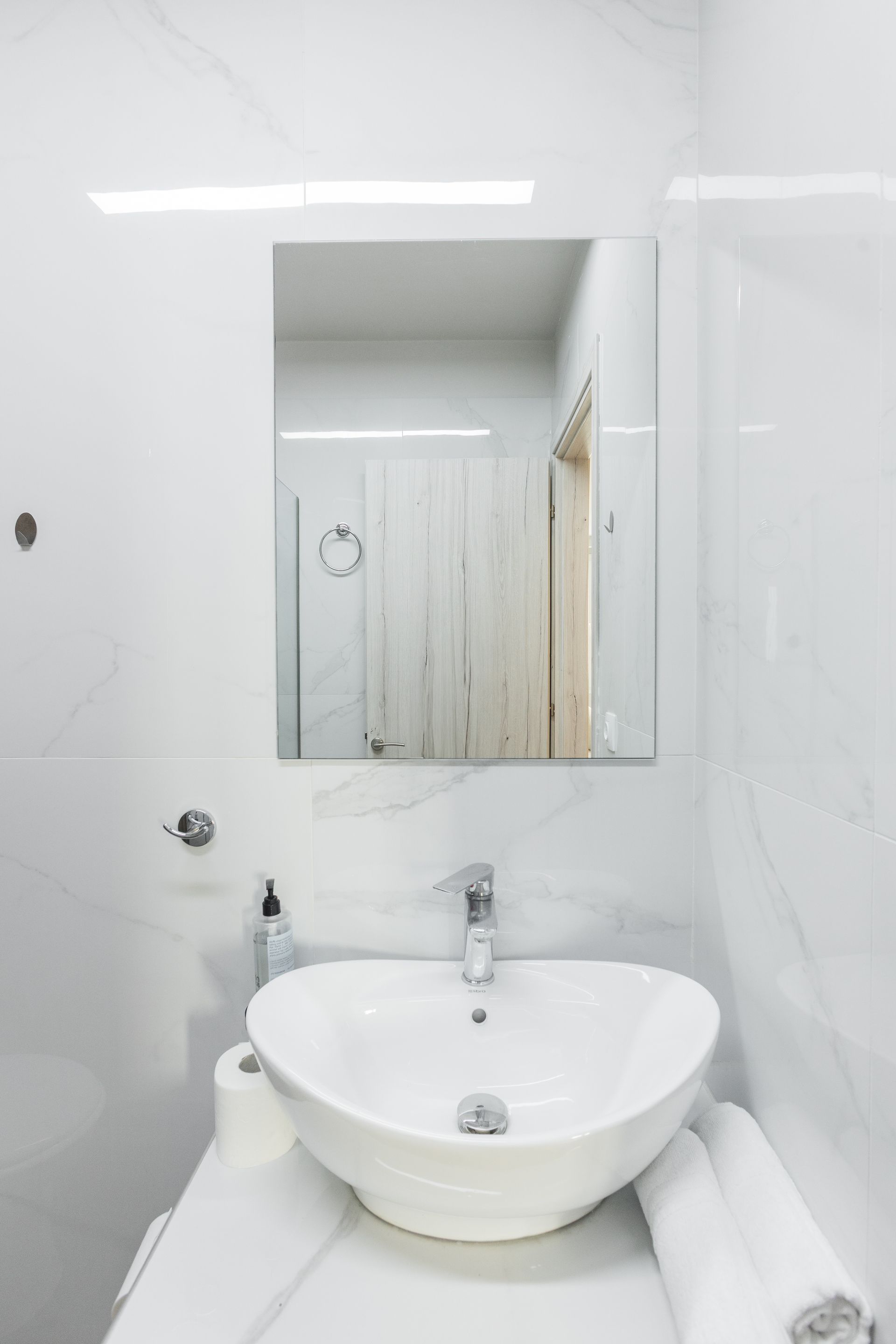 White bathroom with a vessel sink, mirror, and towel rolls on a countertop.