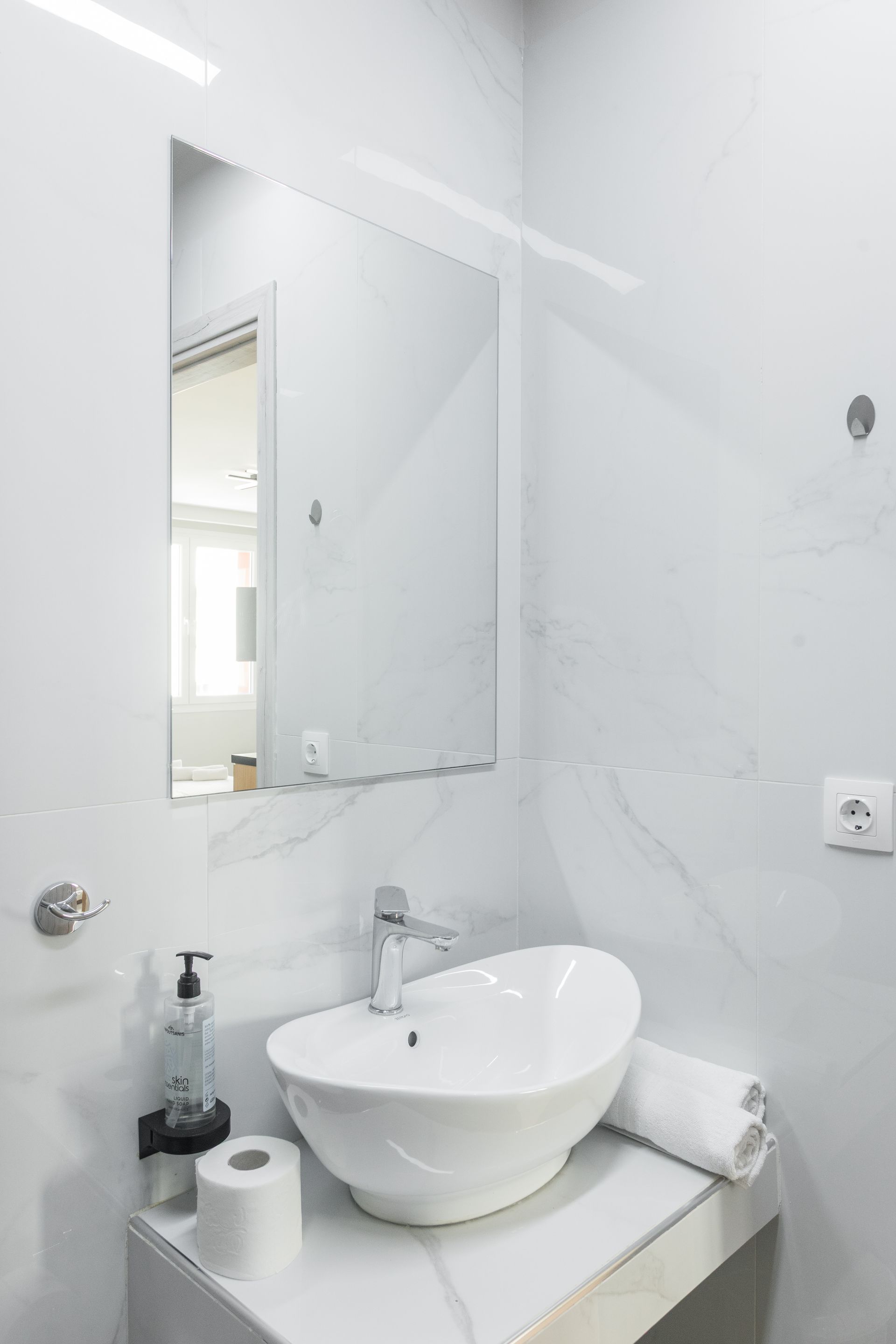 Modern white bathroom with a vessel sink, mirror, and marble-like tile.