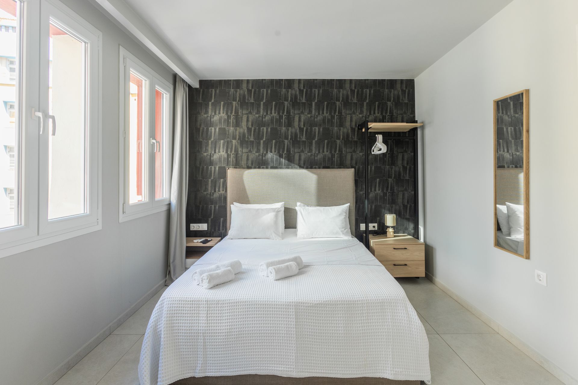Bedroom with bed, nightstands, windows, and decorative wallpaper.