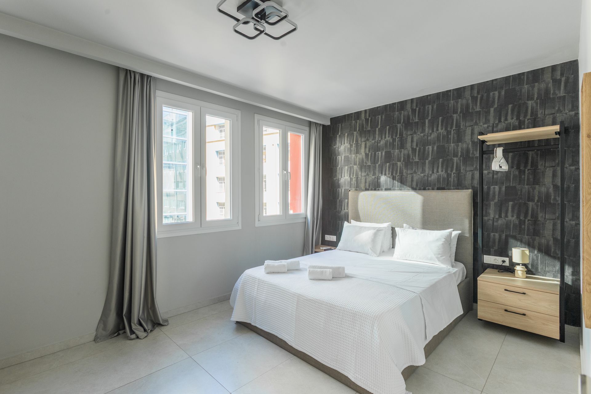 Bedroom with double bed, windows, dark wallpaper, and light wooden bedside table.