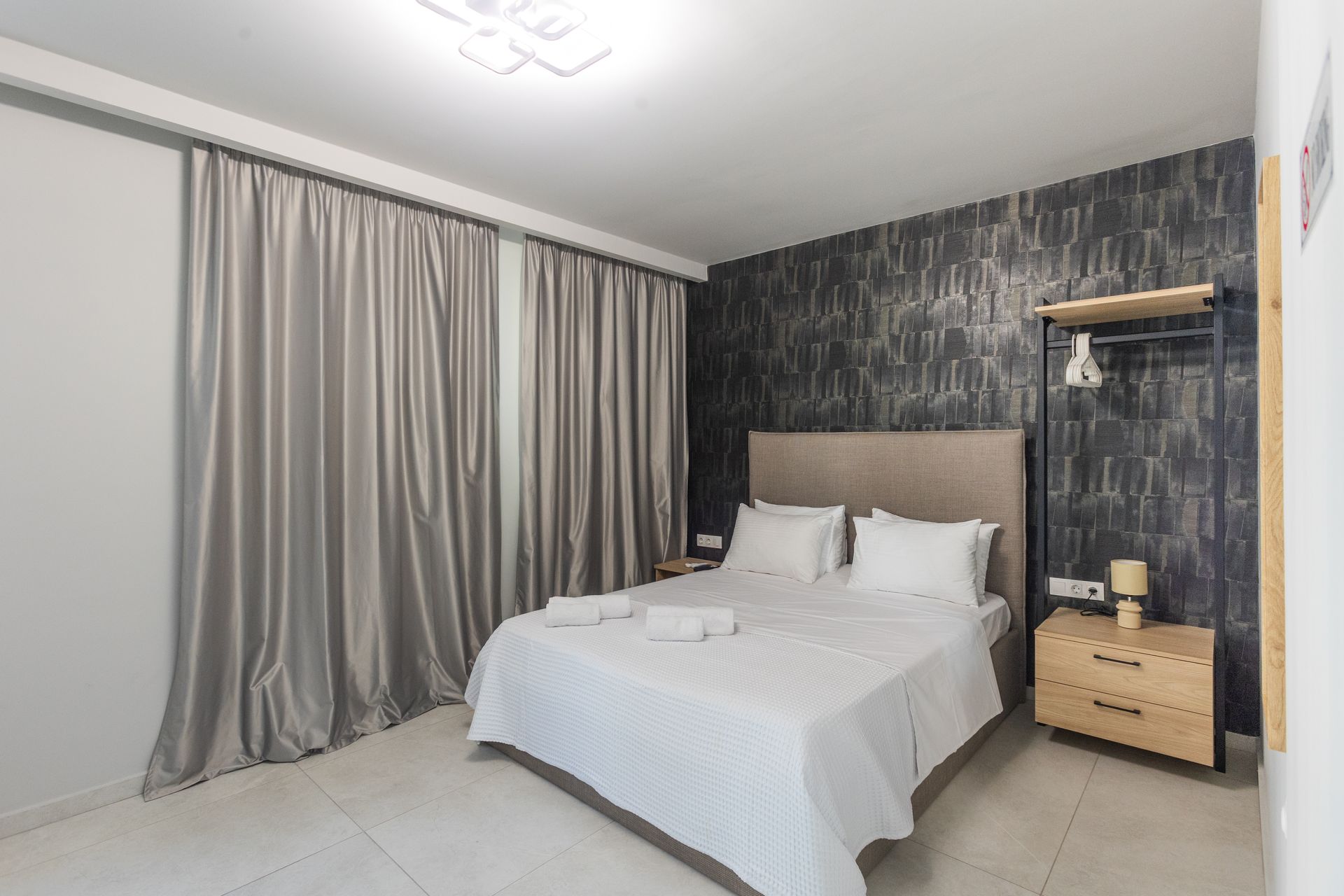 Bedroom with gray curtains, a bed with white linens, and a wooden nightstand.