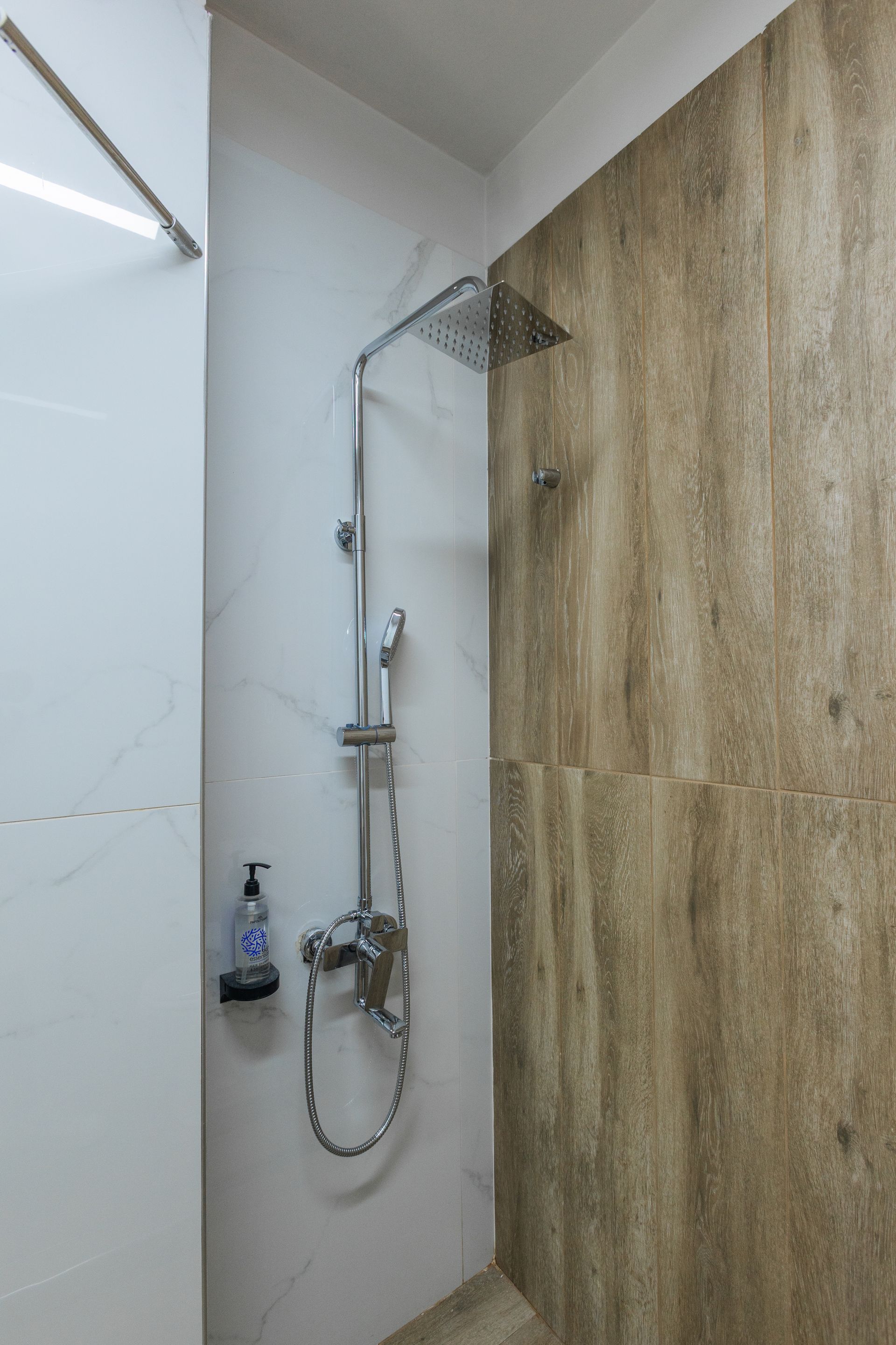 Shower with overhead and handheld fixtures; white and brown tiled walls; soap dispenser.