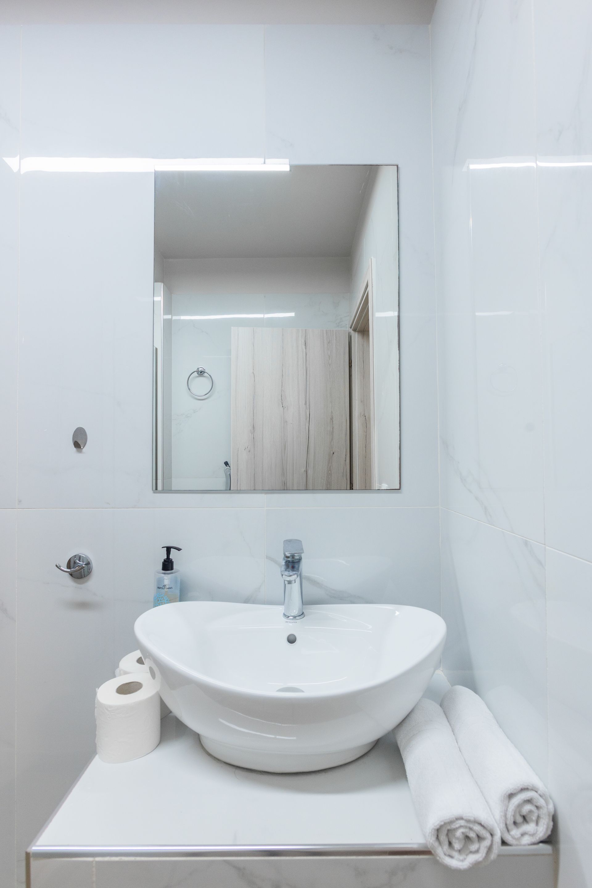 White bathroom with a vessel sink, mirror, and rolled towels.