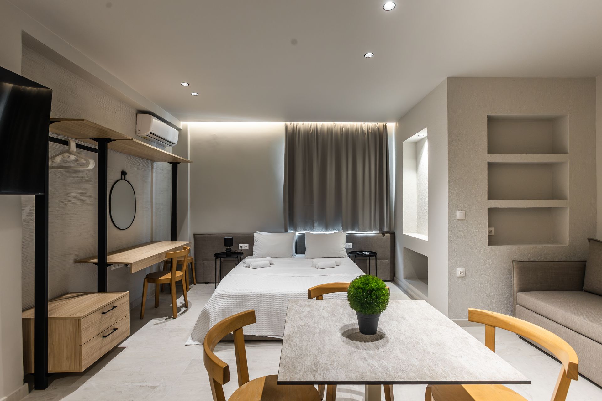 Modern studio apartment with bed, desk, table, and sofa. Neutral color scheme, bright lighting.