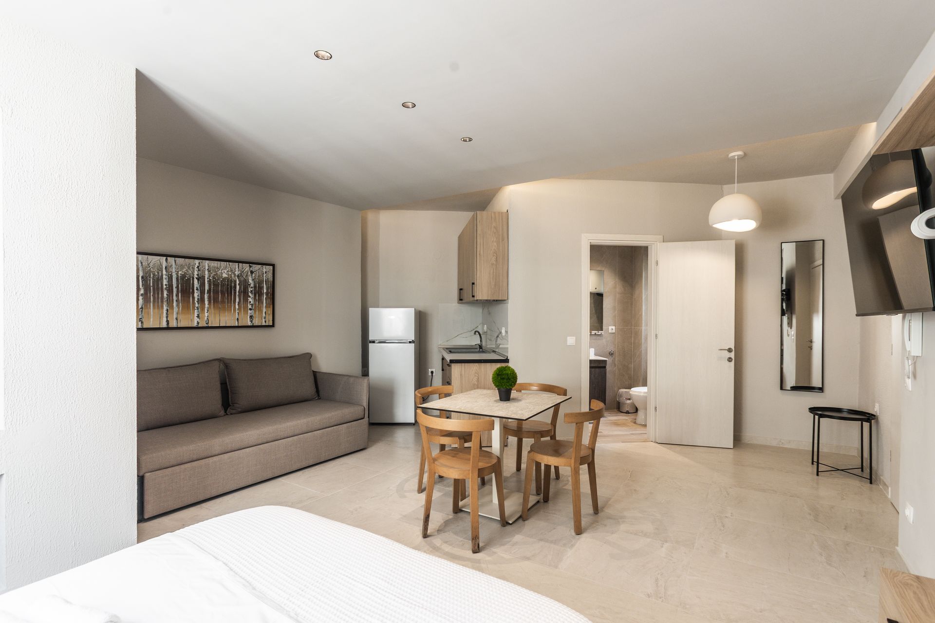 A studio apartment with a kitchenette, dining area, sofa, and a bathroom visible through an open doorway.