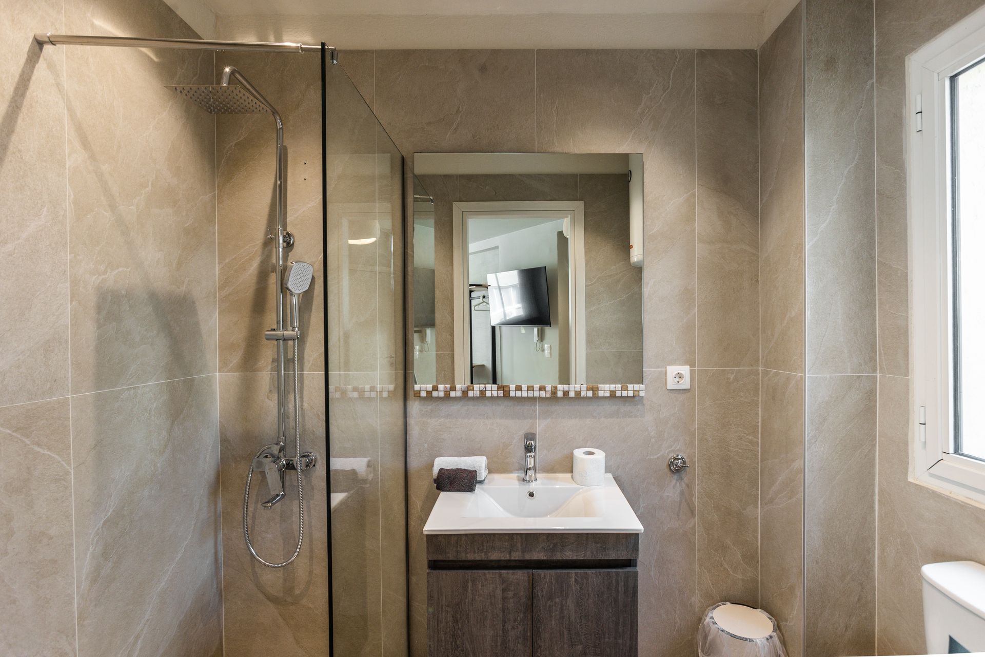 Bathroom with shower, vanity, and mirror. Beige tile walls, glass shower door, and a small window.