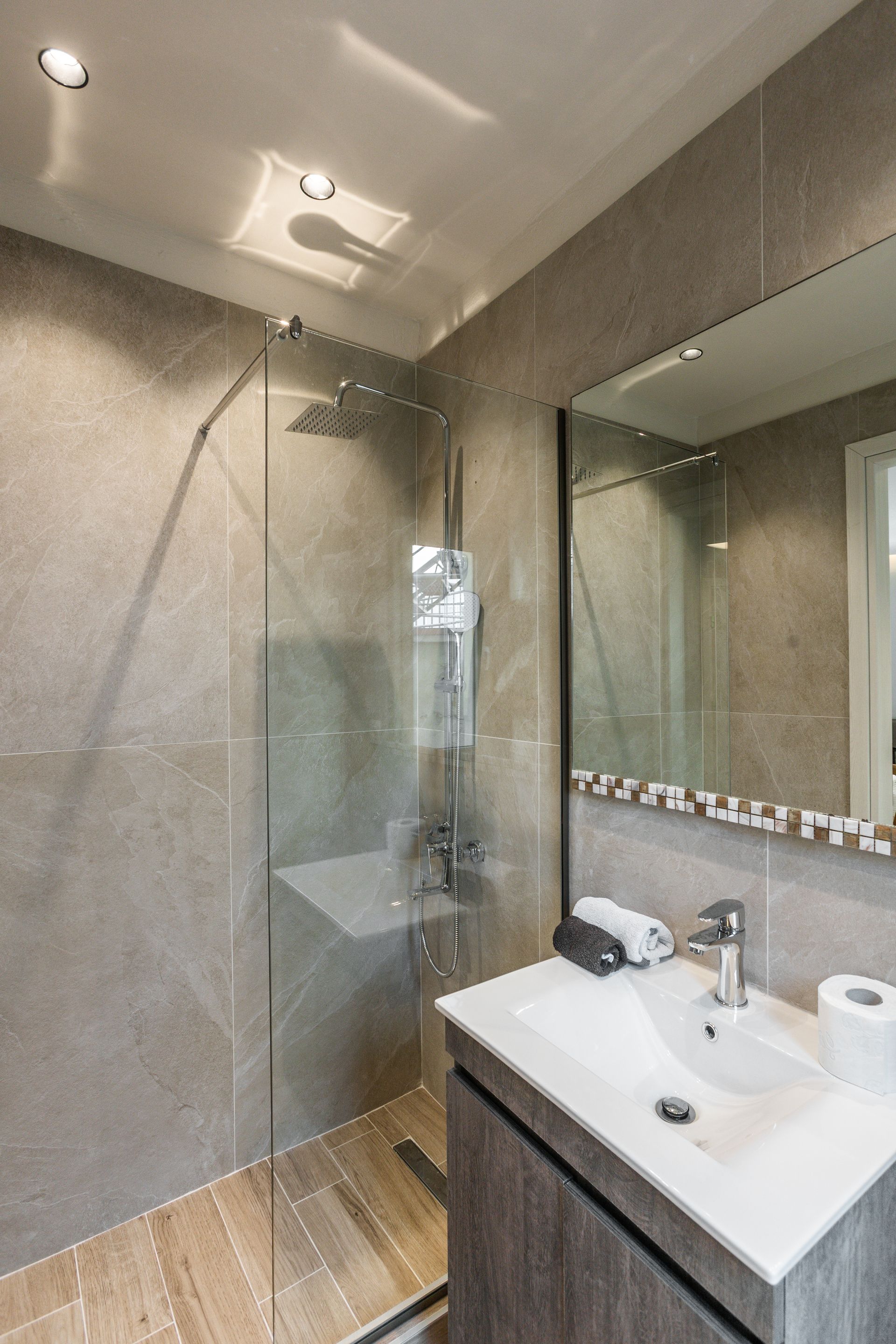 Bathroom with gray tile, glass shower, vanity, and large mirror.