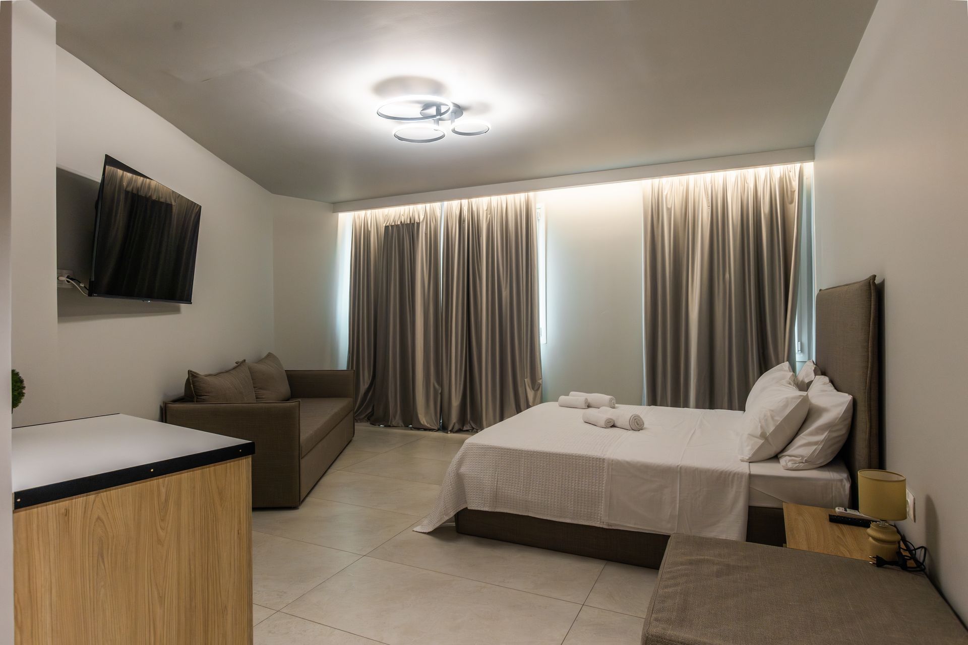 Modern hotel room with a bed, sofa, TV, and large window with curtains.