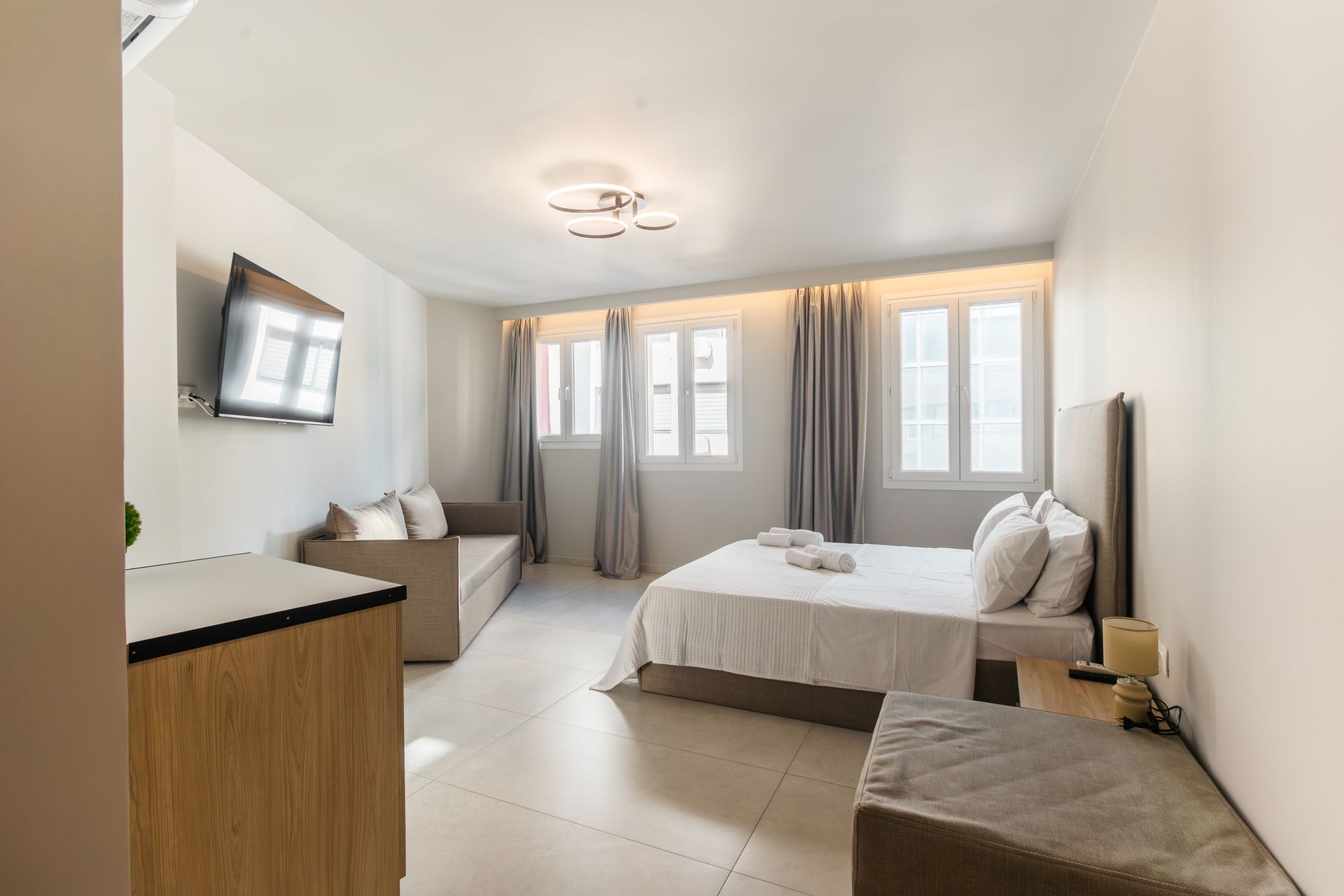 Brightly lit studio apartment with a bed, sofa, and TV.