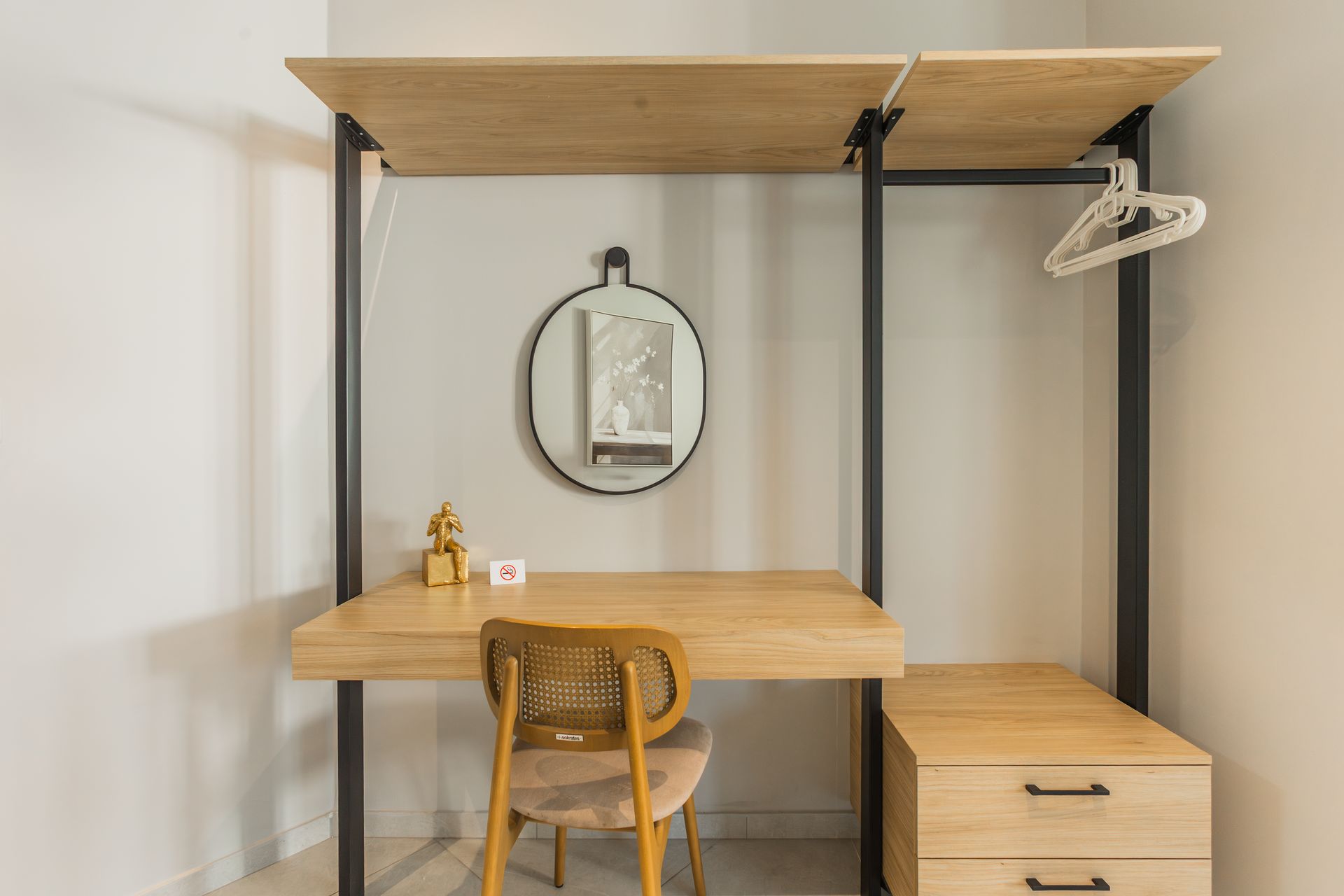 Wooden desk with chair, closet and drawers, mirror, and decorations against a white wall.