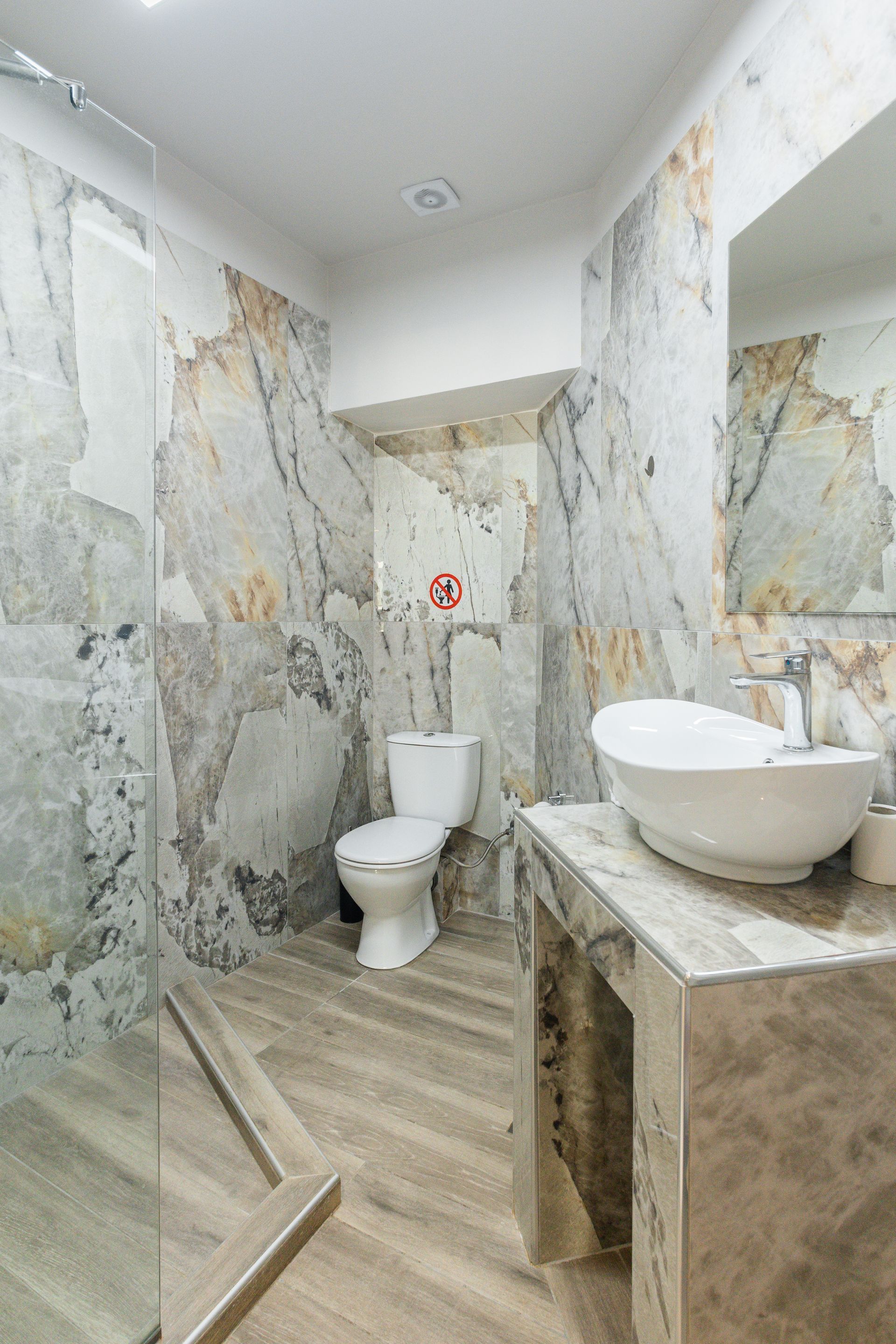 Bathroom with marble walls, toilet, vessel sink, and glass shower door.