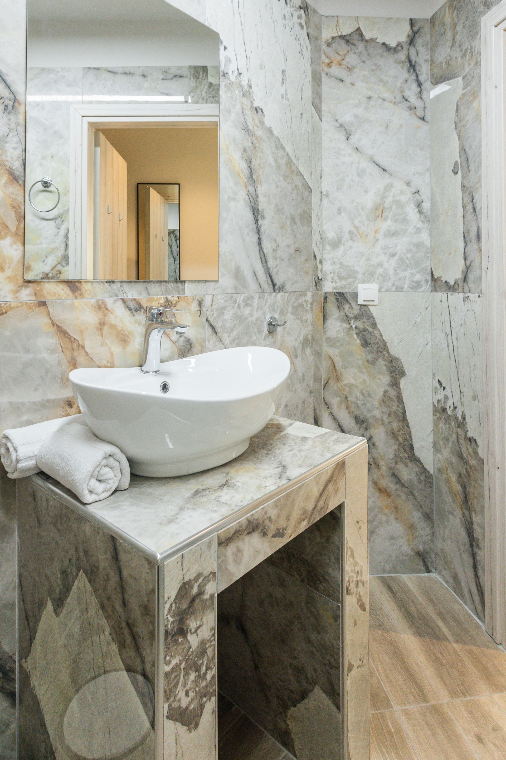 White vessel sink on a marble countertop in a bathroom with marble walls and wood floor.