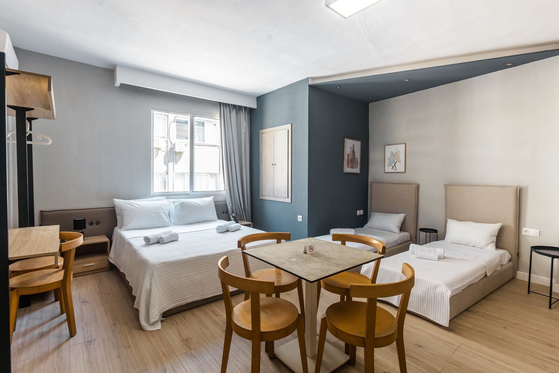 Hotel room with double and single beds, table with chairs, and neutral color scheme.