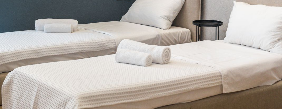 Two neatly made twin beds with white linens and towels. A small table is between the beds.