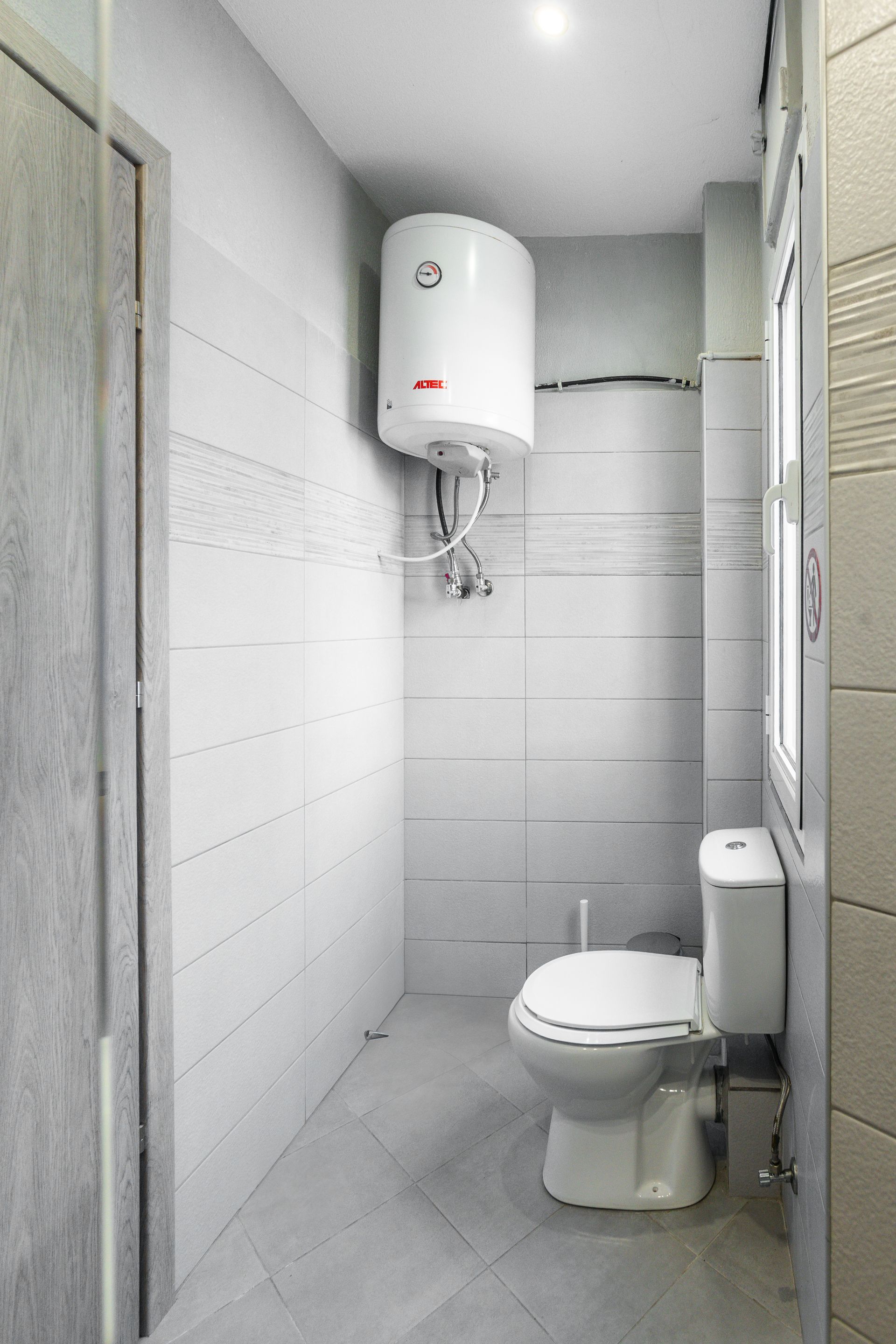 Small bathroom with white tiled walls, toilet, and water heater.