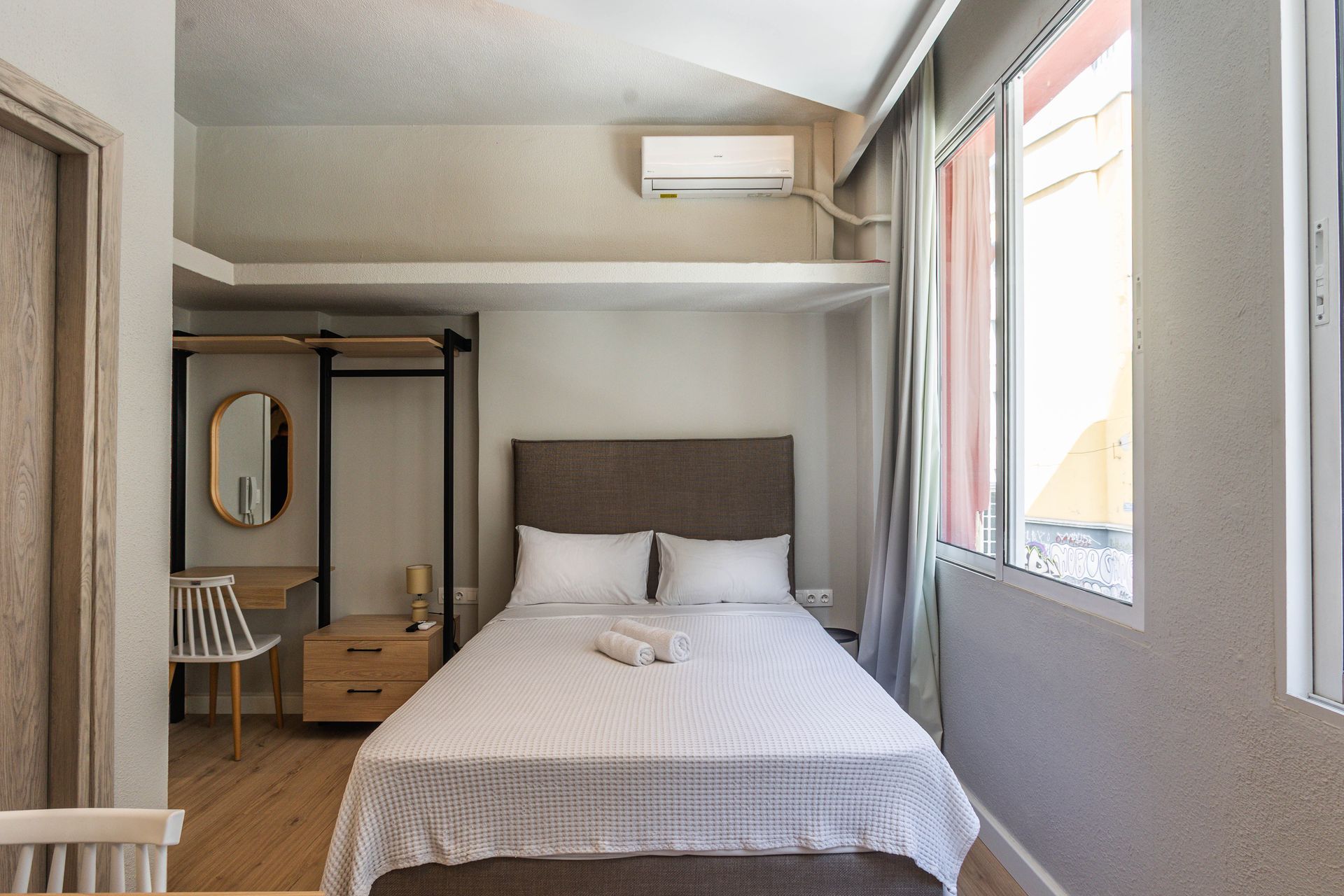 Bedroom with bed, nightstand, desk, and large window.