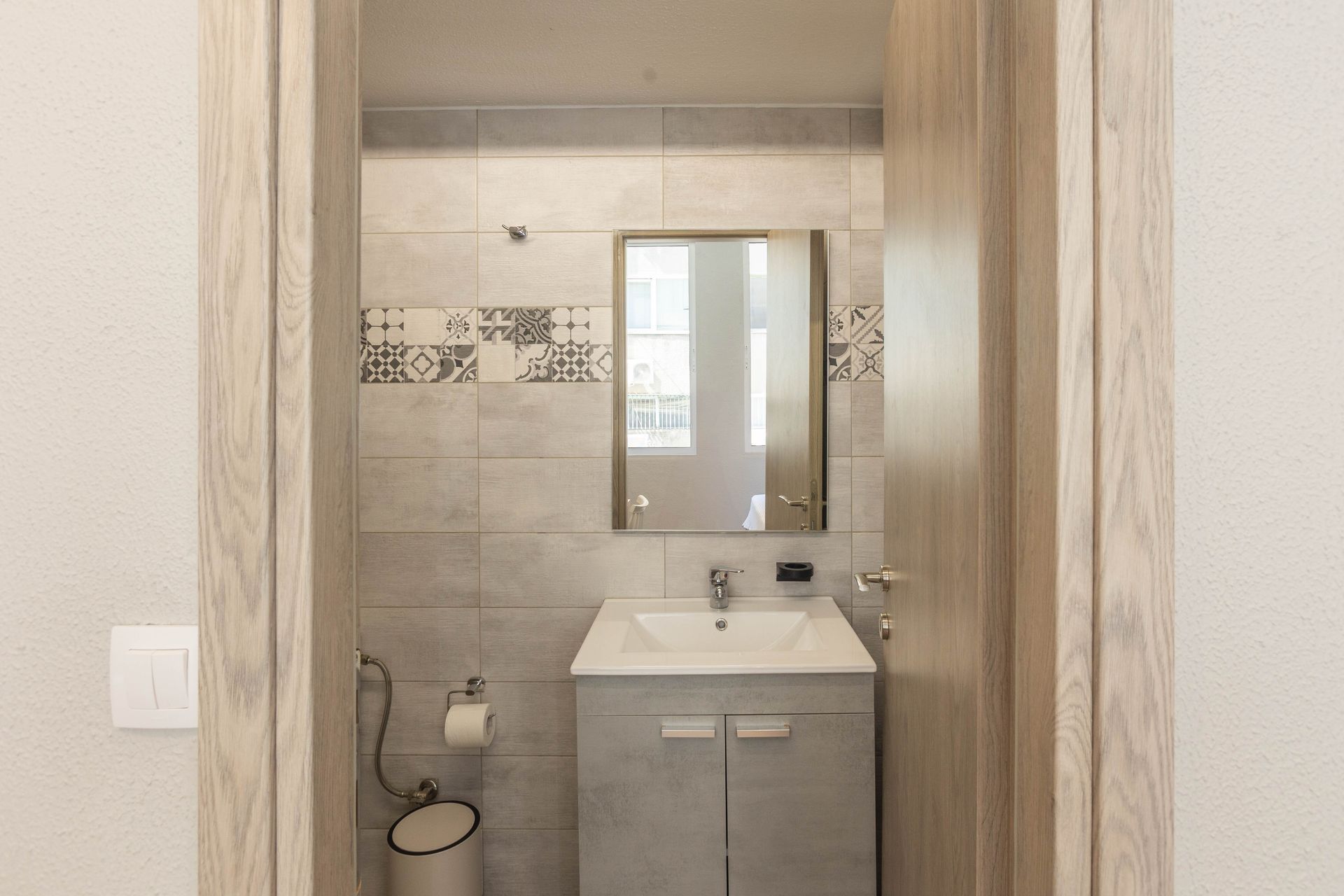 Bathroom with gray tile, a vanity, mirror, and open doorframe.