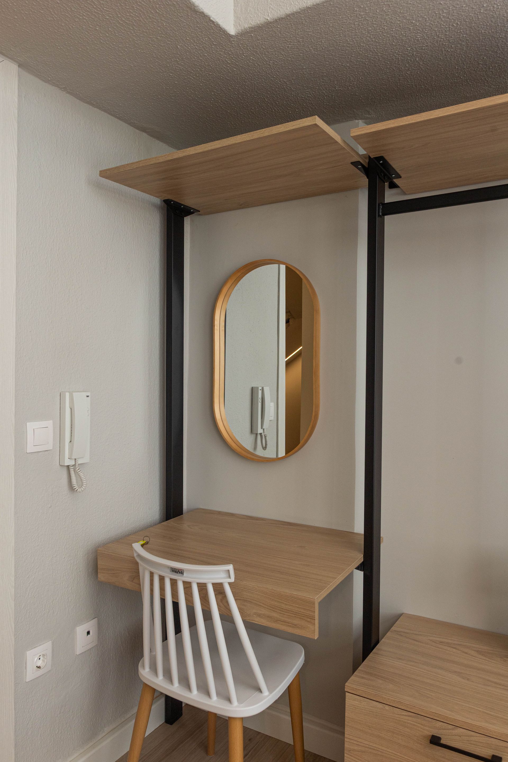 Desk with oval mirror, chair, and shelf in front of a wardrobe unit; light wood and black metal frame.