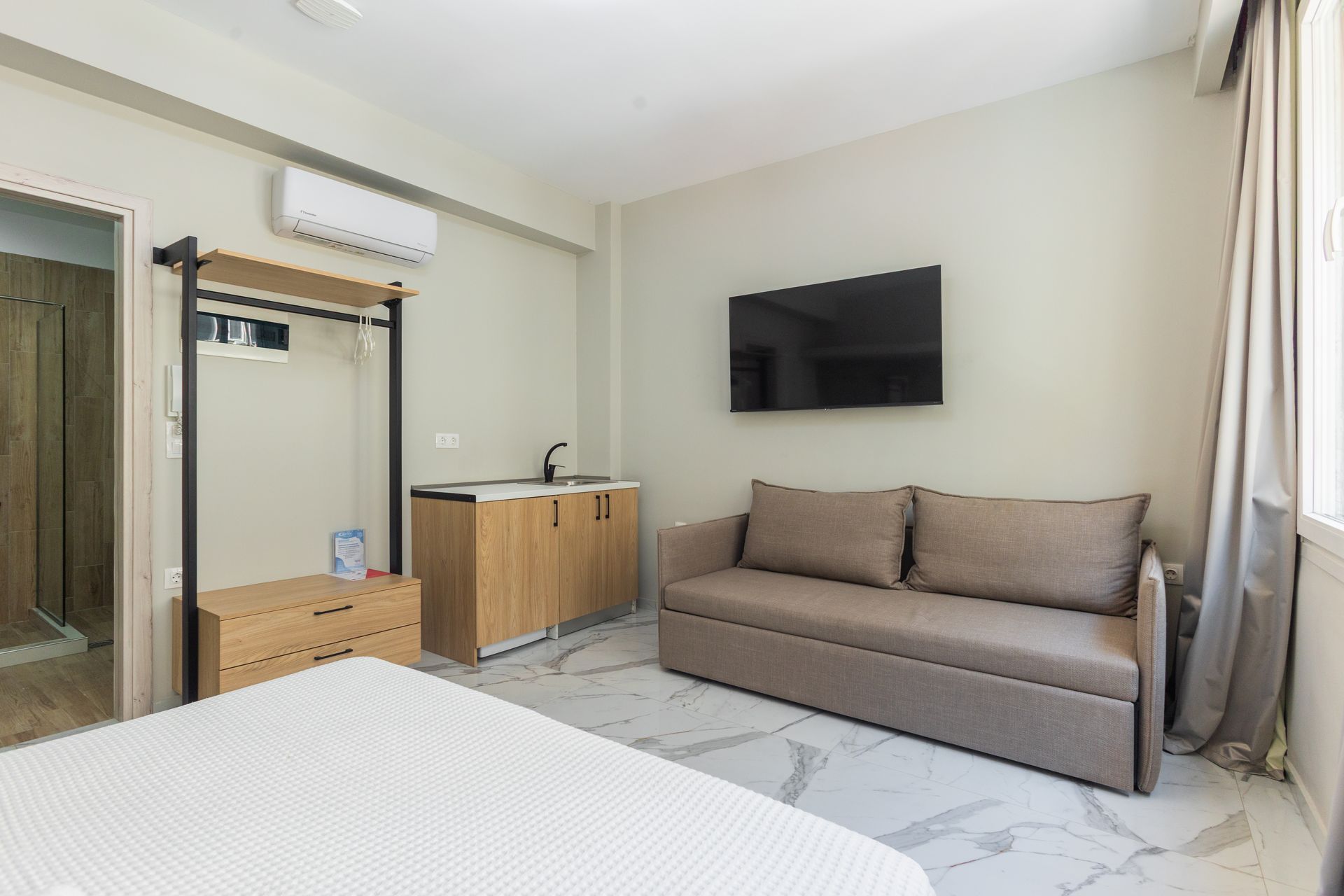 Studio apartment interior with bed, sofa, TV, kitchenette, and window.