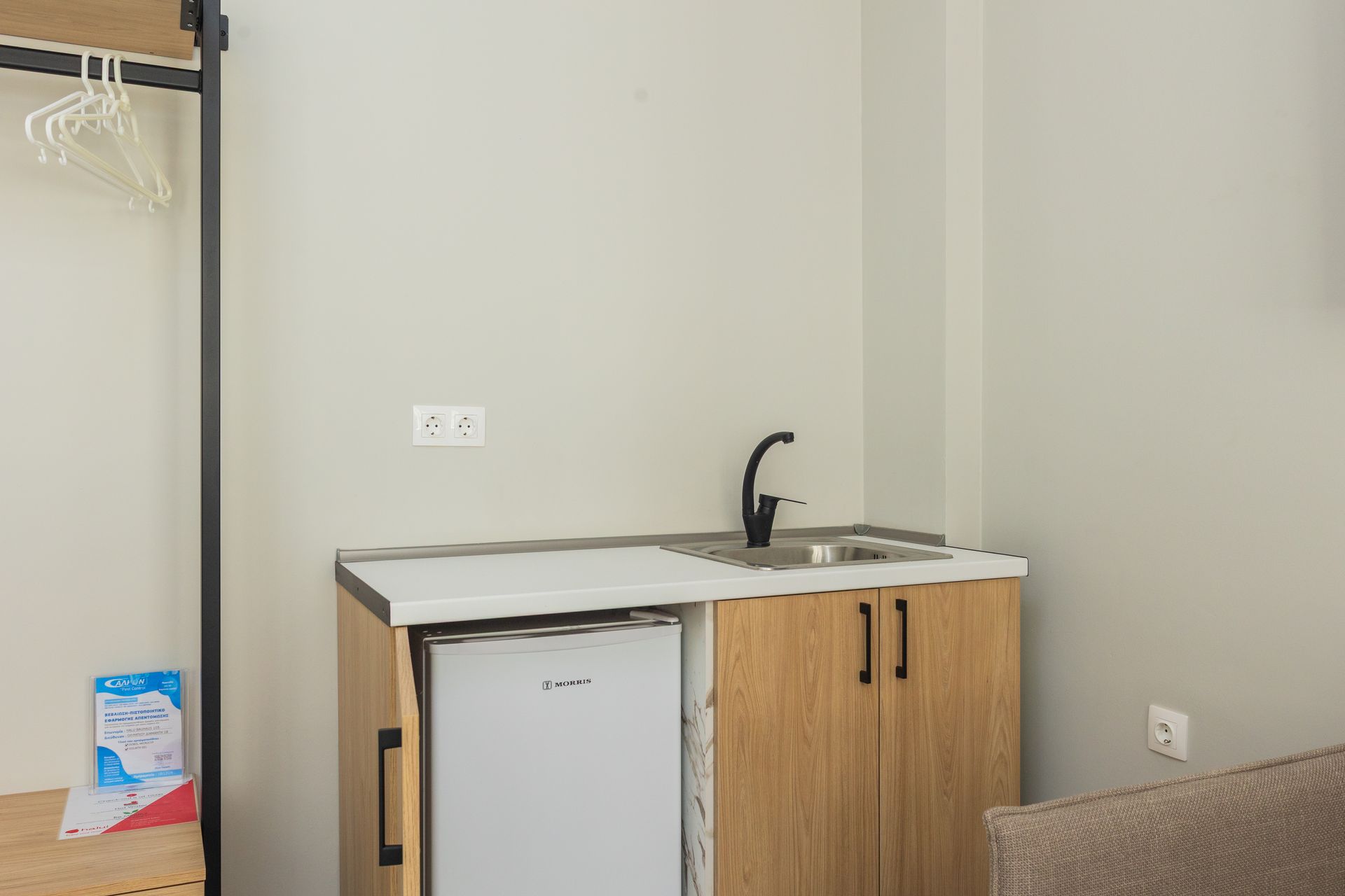 Small kitchenette with sink, mini-fridge, and cabinets in a room. Beige walls, black faucet.