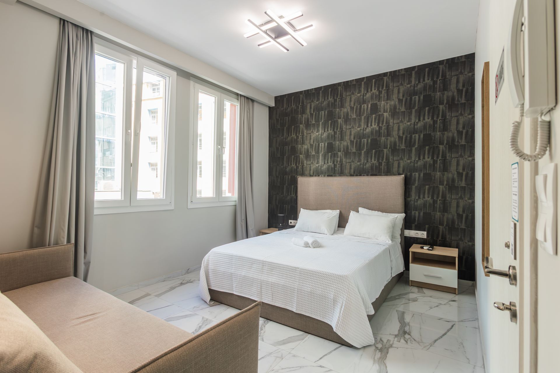 Bedroom with bed, sofa, large windows, and dark textured accent wall.