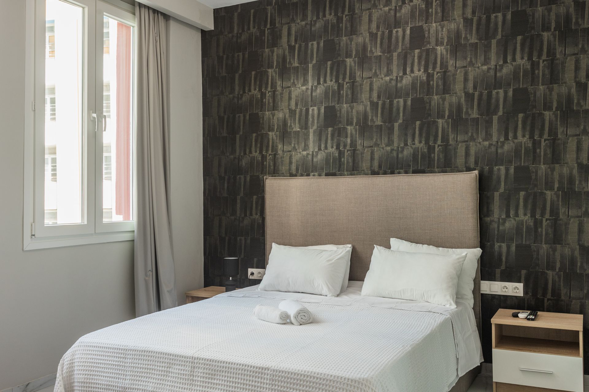 Bedroom with bed, white bedding, nightstands, window, and patterned wallpaper.
