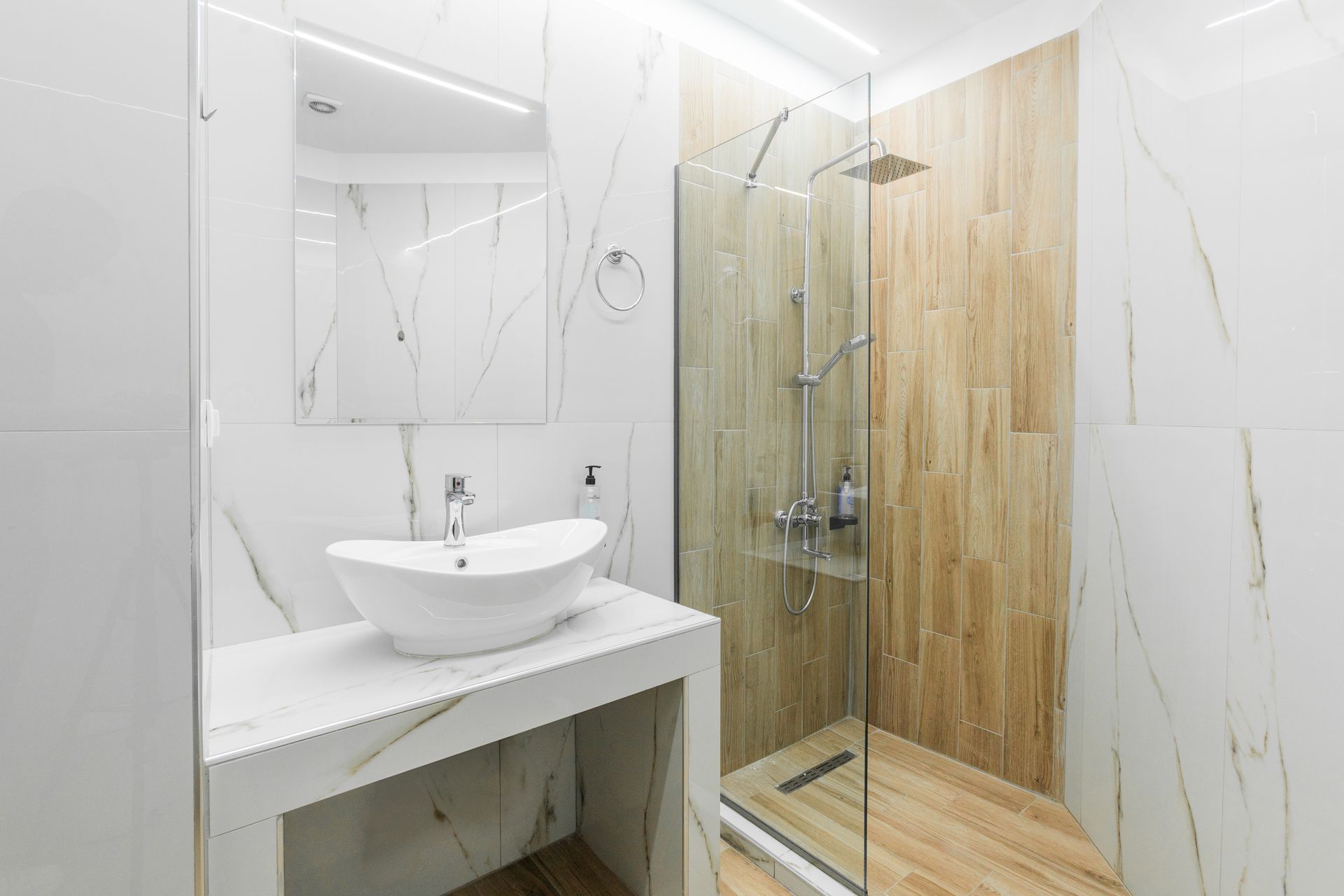 Modern bathroom with marble-look walls, a vessel sink, glass shower, and wood-like accent wall.