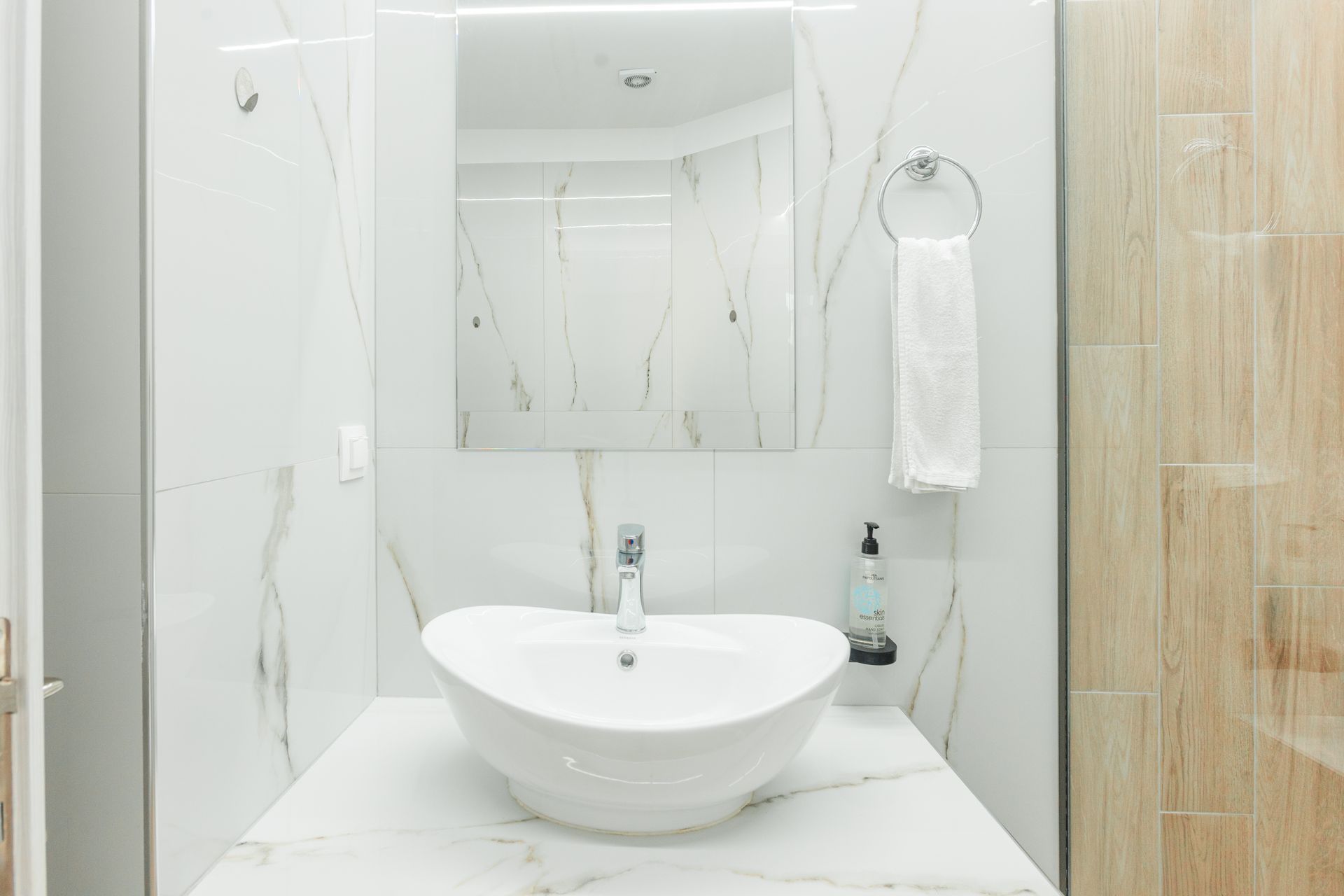 Bathroom with a white vessel sink on a marble countertop, mirror, towel, and light-colored tile.
